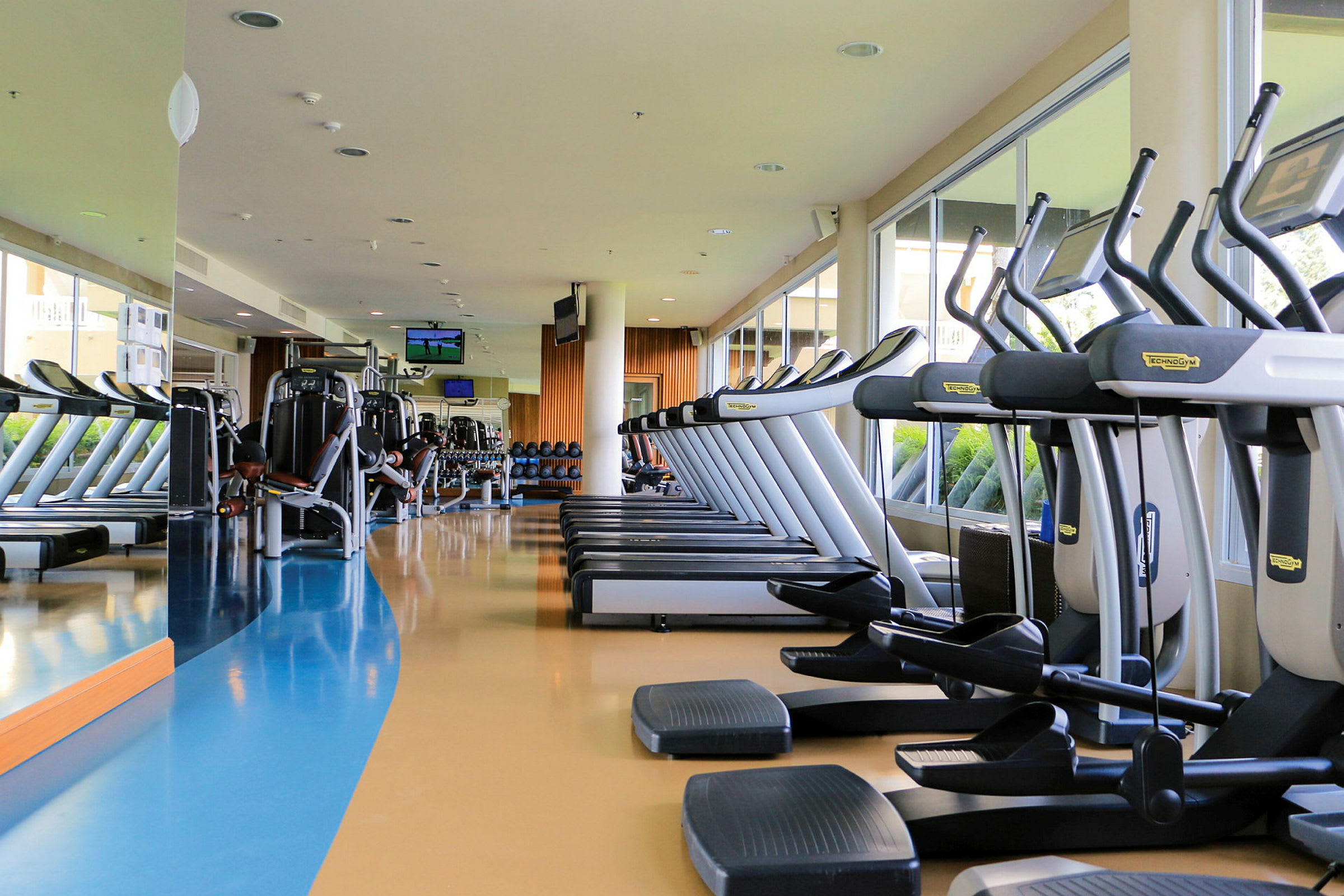 Ett gym med träningsmaskiner och löpband vid fönster. (AI-genererad text)