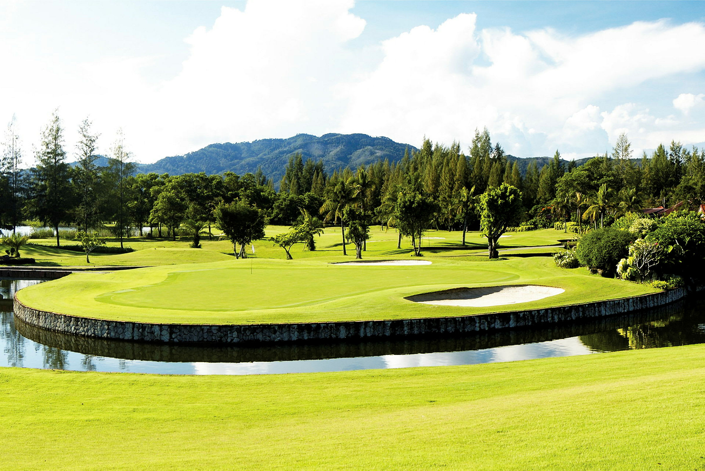 En golfbana med grön fairway, vattenhinder och bunkrar, omliggande träd och berg i bakgrunden. (AI-genererad text)