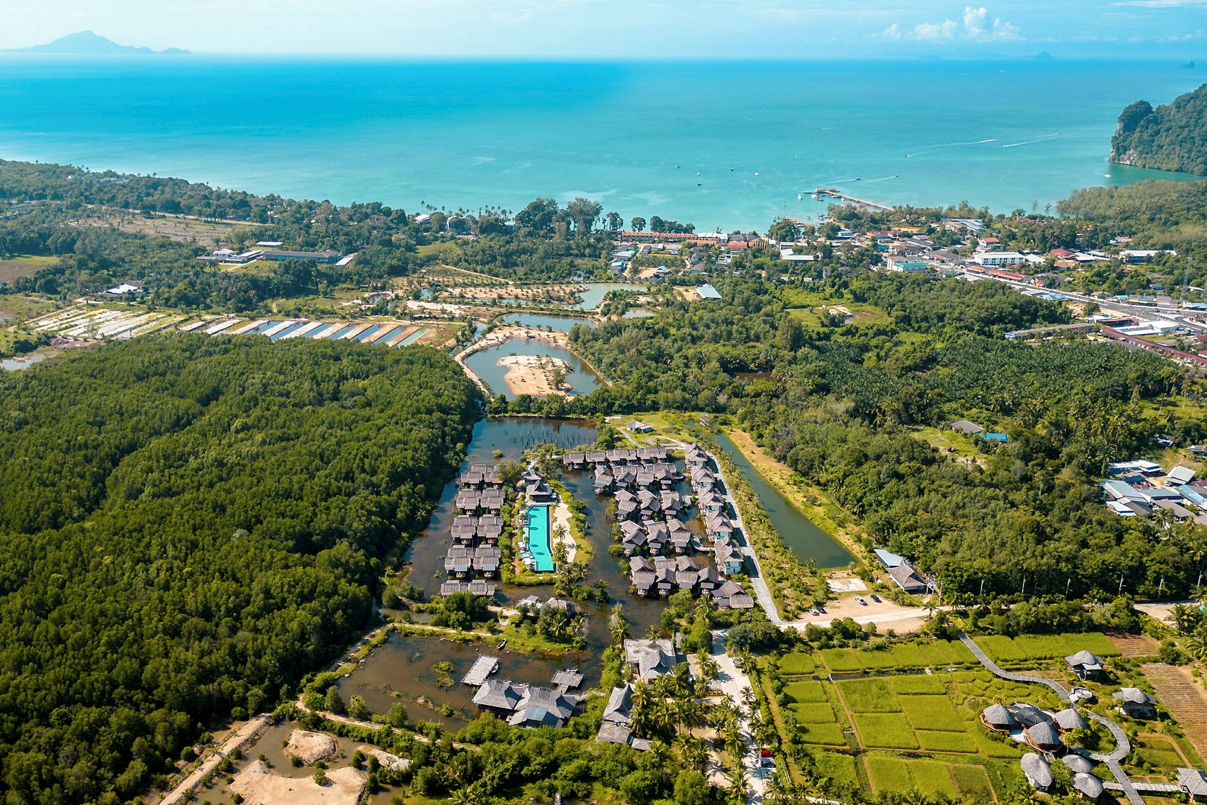 Flygbild över ett resortområde omgiven av vegetation, med en swimmingpool i centrum och havet i bakgrunden. (AI-genererad text)