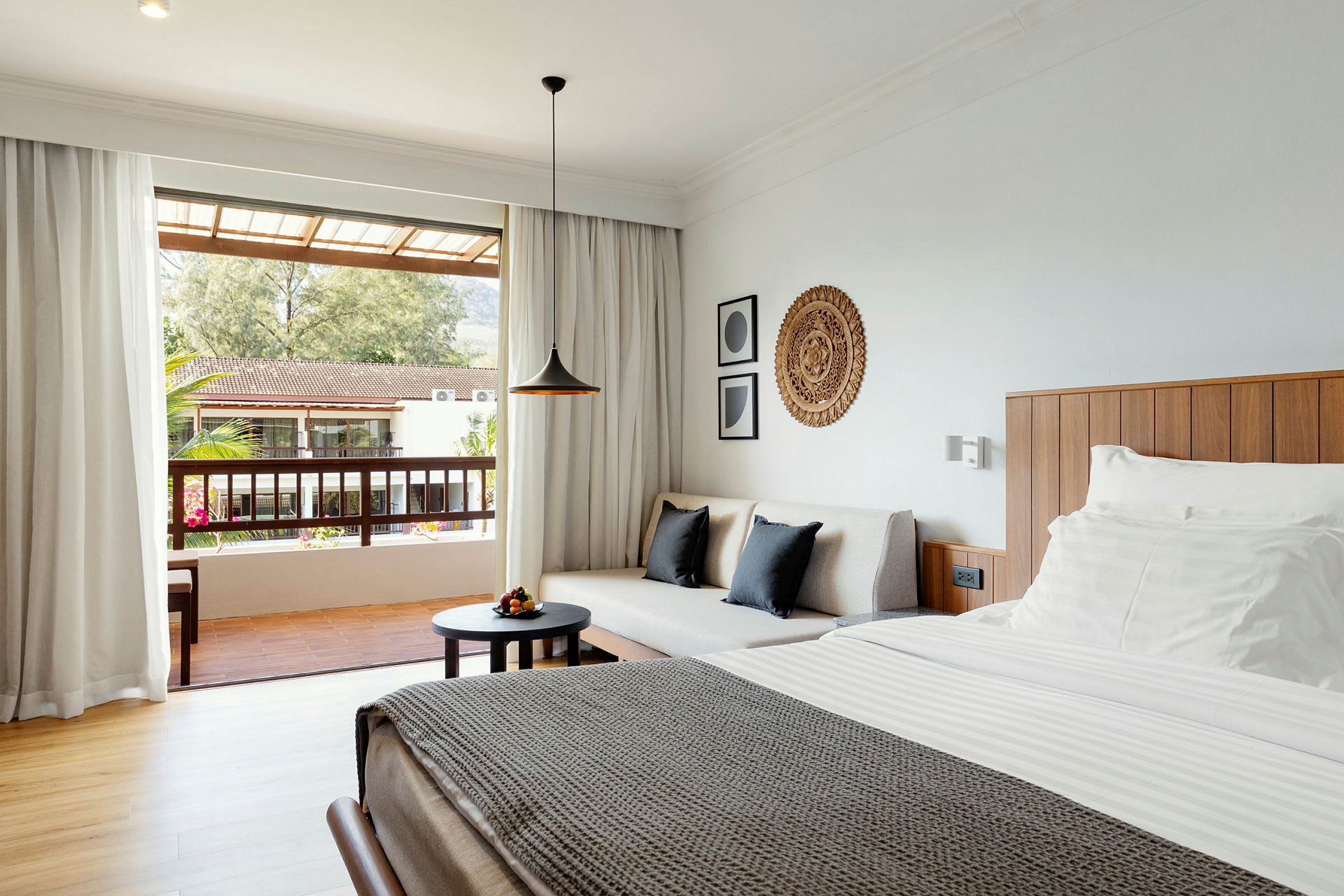 En öppen hotellrum med en soffa och en säng med vita lakan, utsikt från balkongen mot ett bostadsområde. (AI-genererad text)