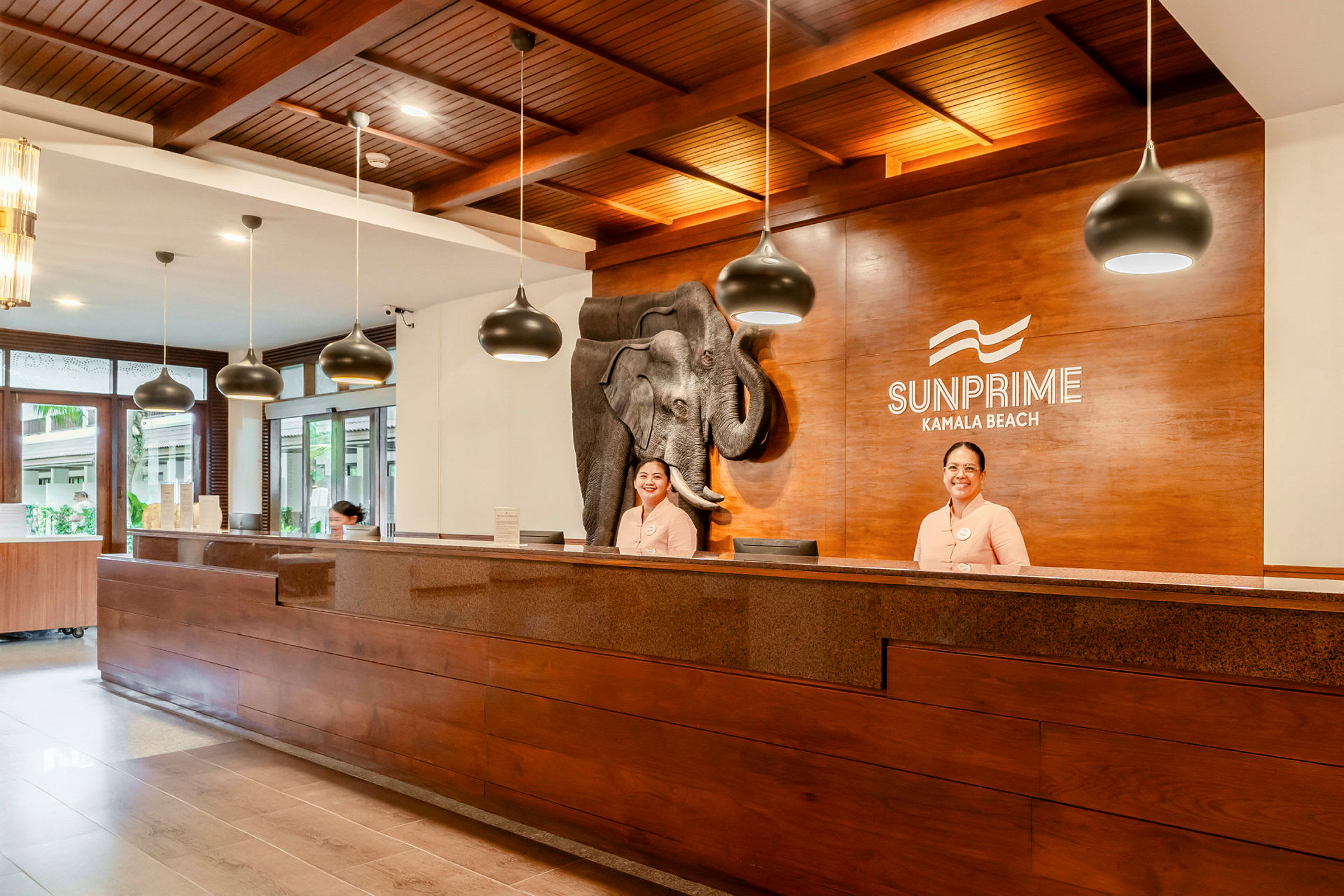 Receptionen på Sunprime Kamala Beach med träinredning och dekorativt elefantmotiv. (AI-genererad text)