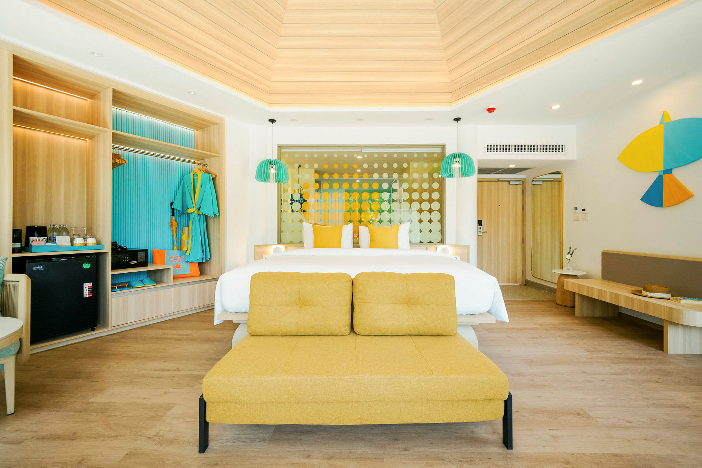 Ett hotellrum med en dubbelsäng, gula kuddförsedda möbler och färgglada detaljer, inklusive kläder på en öppnen garderob och moderna belysningar. (AI-genererad text)