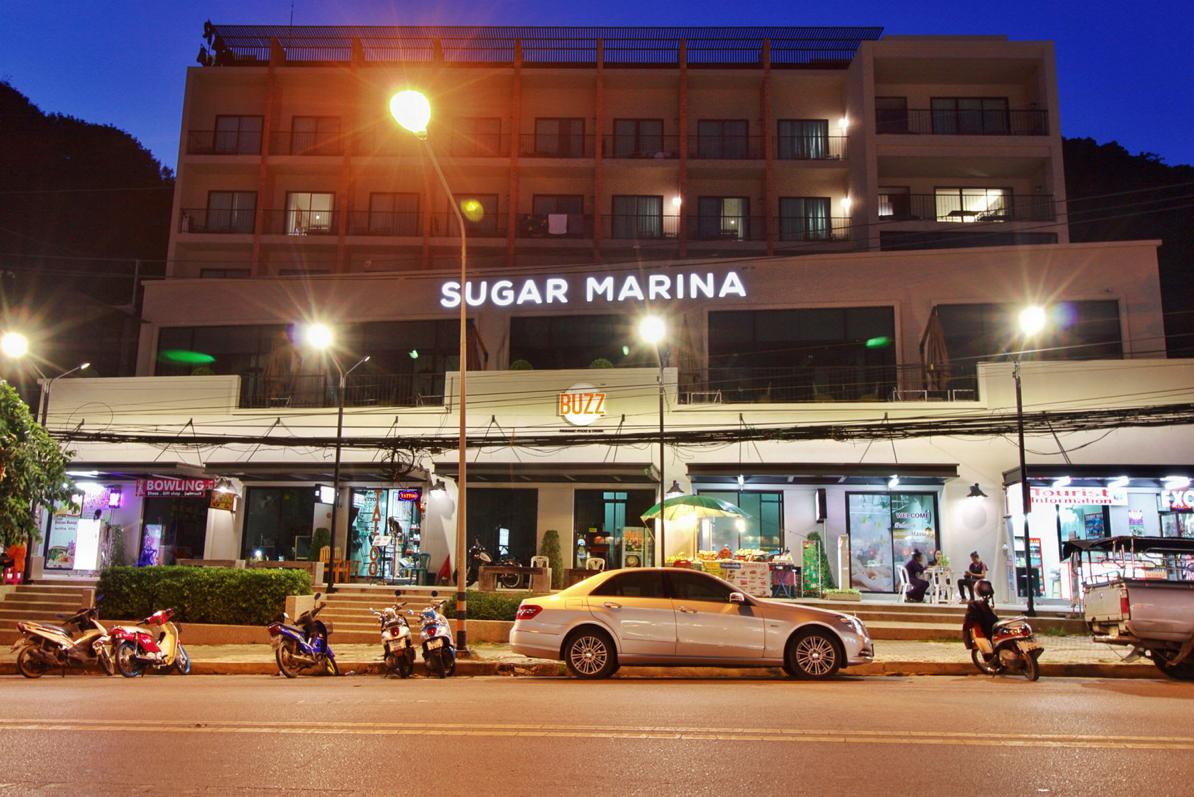Byggnad med hotellnamnet Sugar Marina upplyst på fasaden i natten, med motorcyklar och bilar parkerade vid gatan. (AI-genererad text)