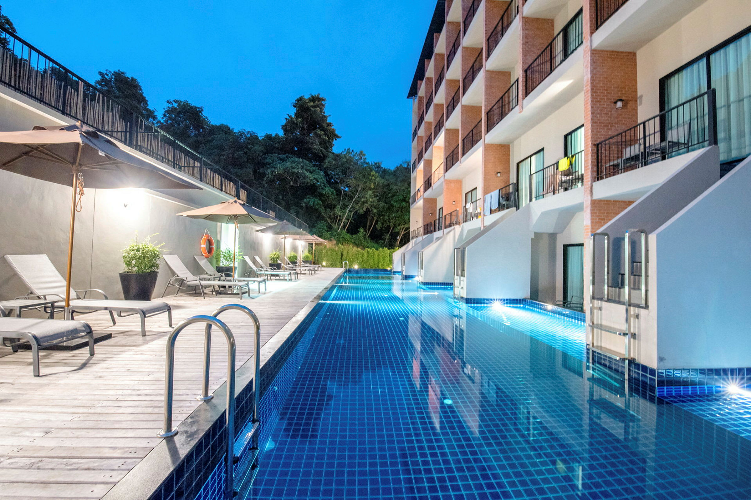 En lång swimmingpool vid ett hotell med solstolar och parasoller längs ena sidan. (AI-genererad text)