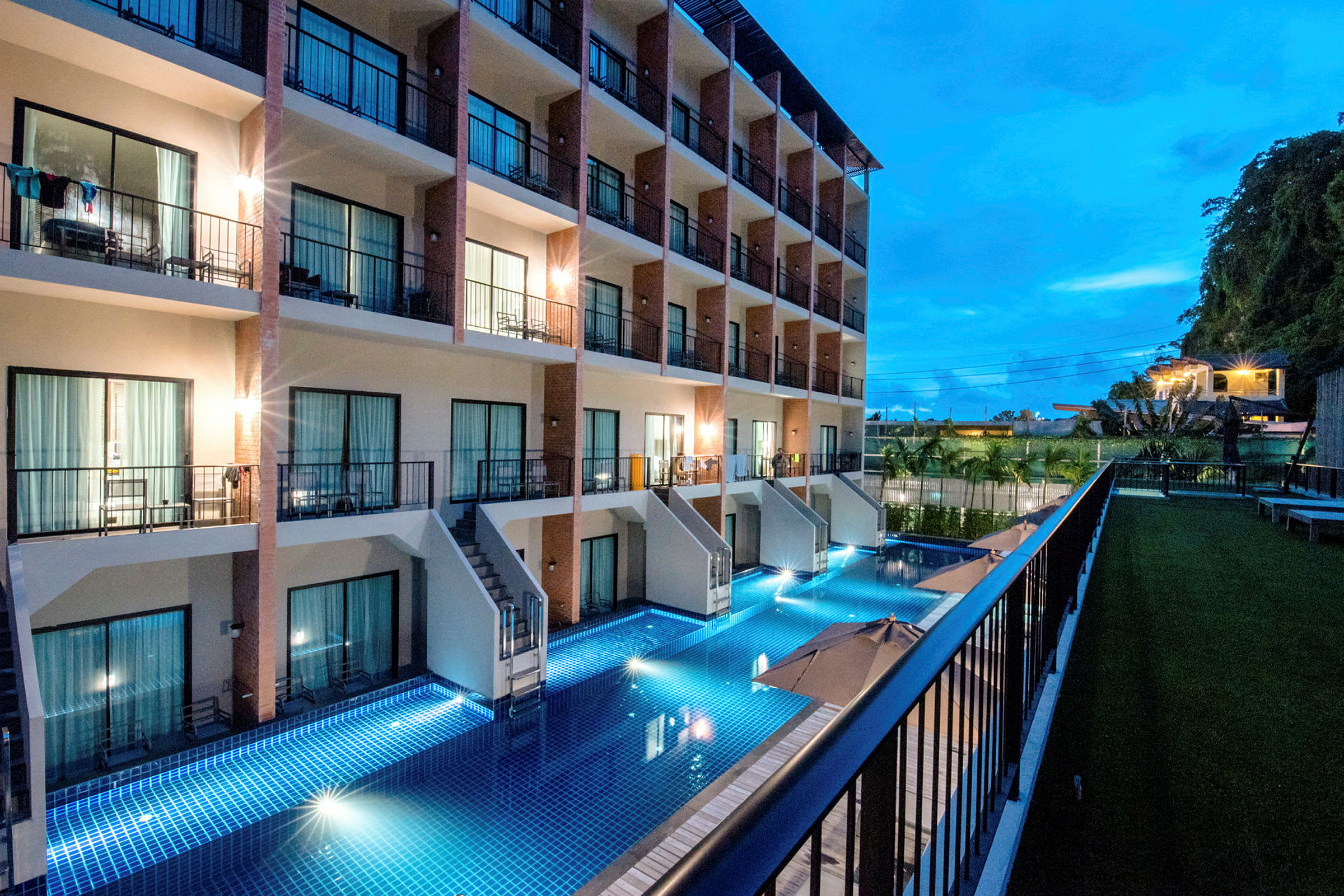 Ett hotell under kvällstid med en pool vid dess fasad och balkonger tillhörande rummen. (AI-genererad text)