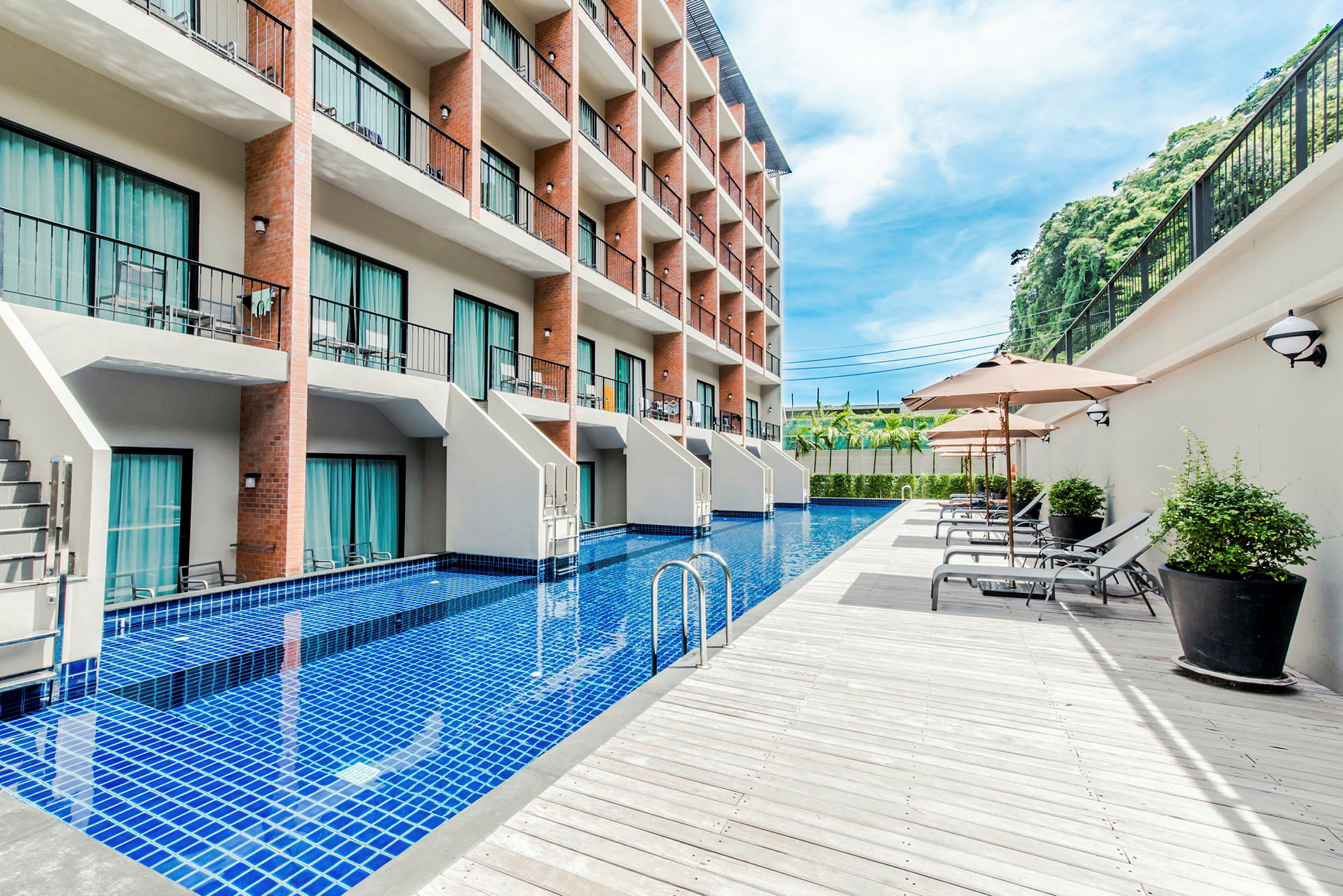 Ett hotell med flera våningar och en lång pool framför byggnaden, omgiven av solstolar och parasoller. (AI-genererad text)