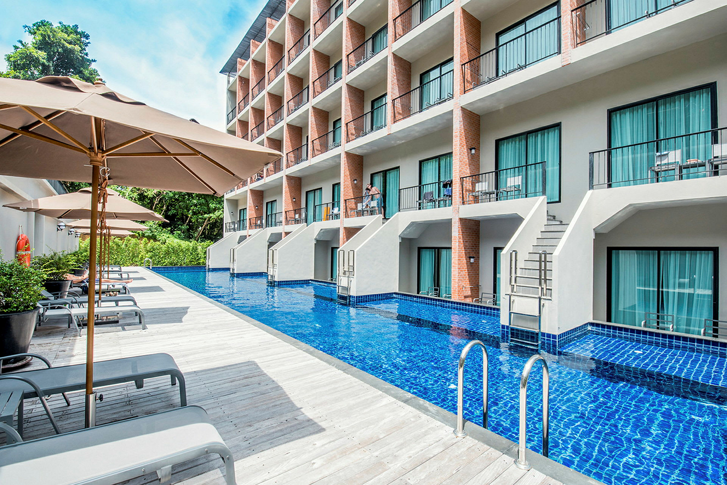 Hotellbyggnad med balkonger och en pool framför, omgiven av solstolar och parasoller. (AI-genererad text)