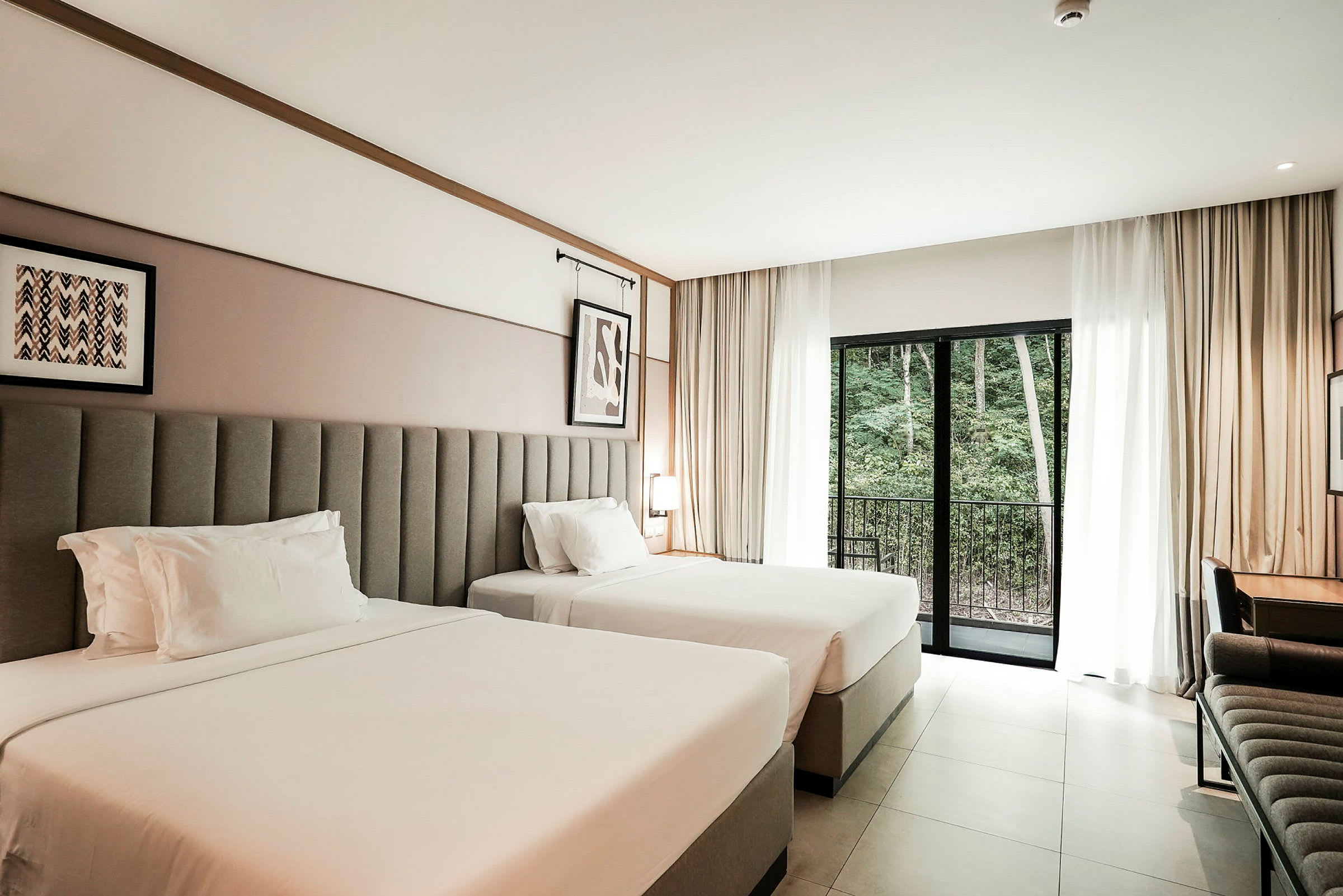 Ett hotellrum med två breda sängar, ett skrivbord och en balkongdörr med utsikt över skogsområde. (AI-genererad text)