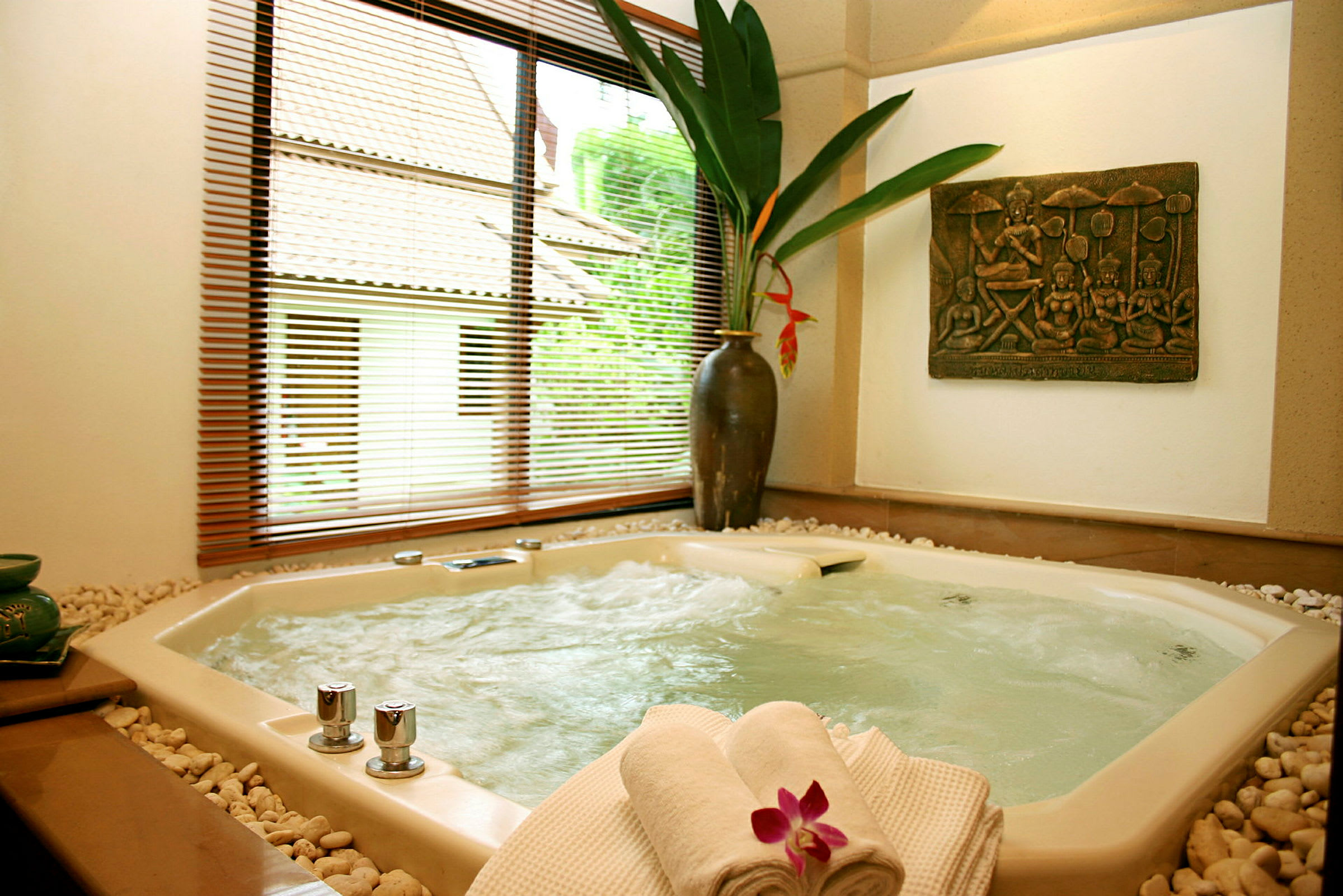 En jacuzzi i ett avkopplande rum med dekorativa element, inklusive en vas med växt och en handduk med blomma. (AI-genererad text)