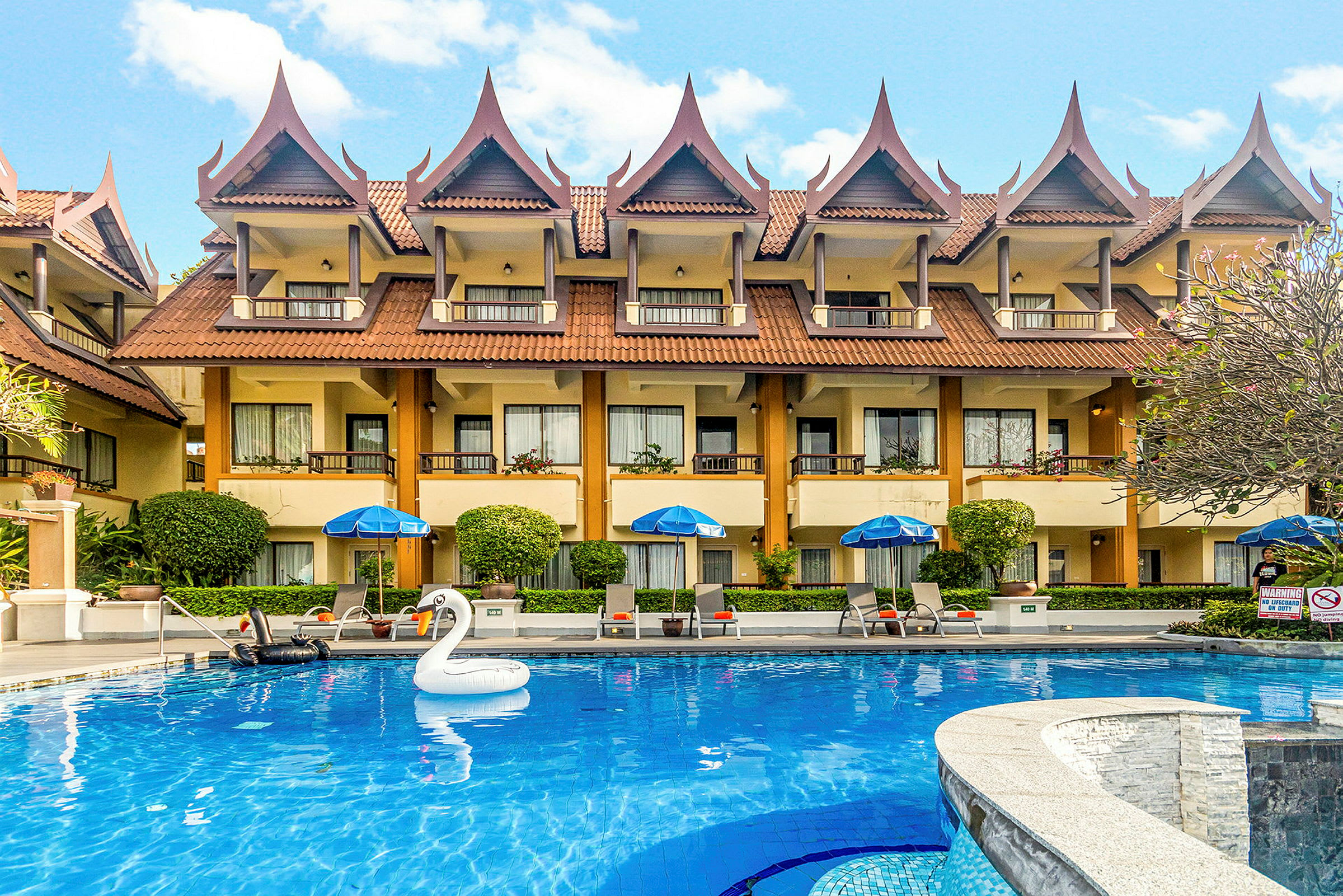 Ett hotell med thailändska takdetaljer och en blå pool framför, inklusive en uppblåsbar svan. (AI-genererad text)