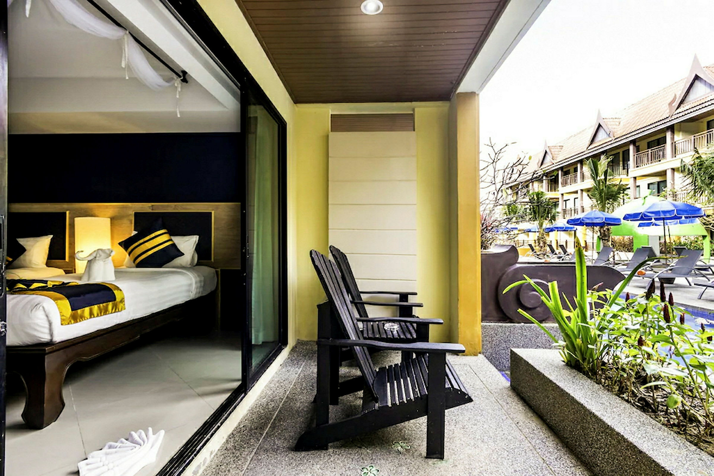 Bild av en hotellterrass med två trästolar som vetter mot en pool med parasoller och solsängar. Hotellets rum syns genom en skjutdörr. (AI-genererad text)