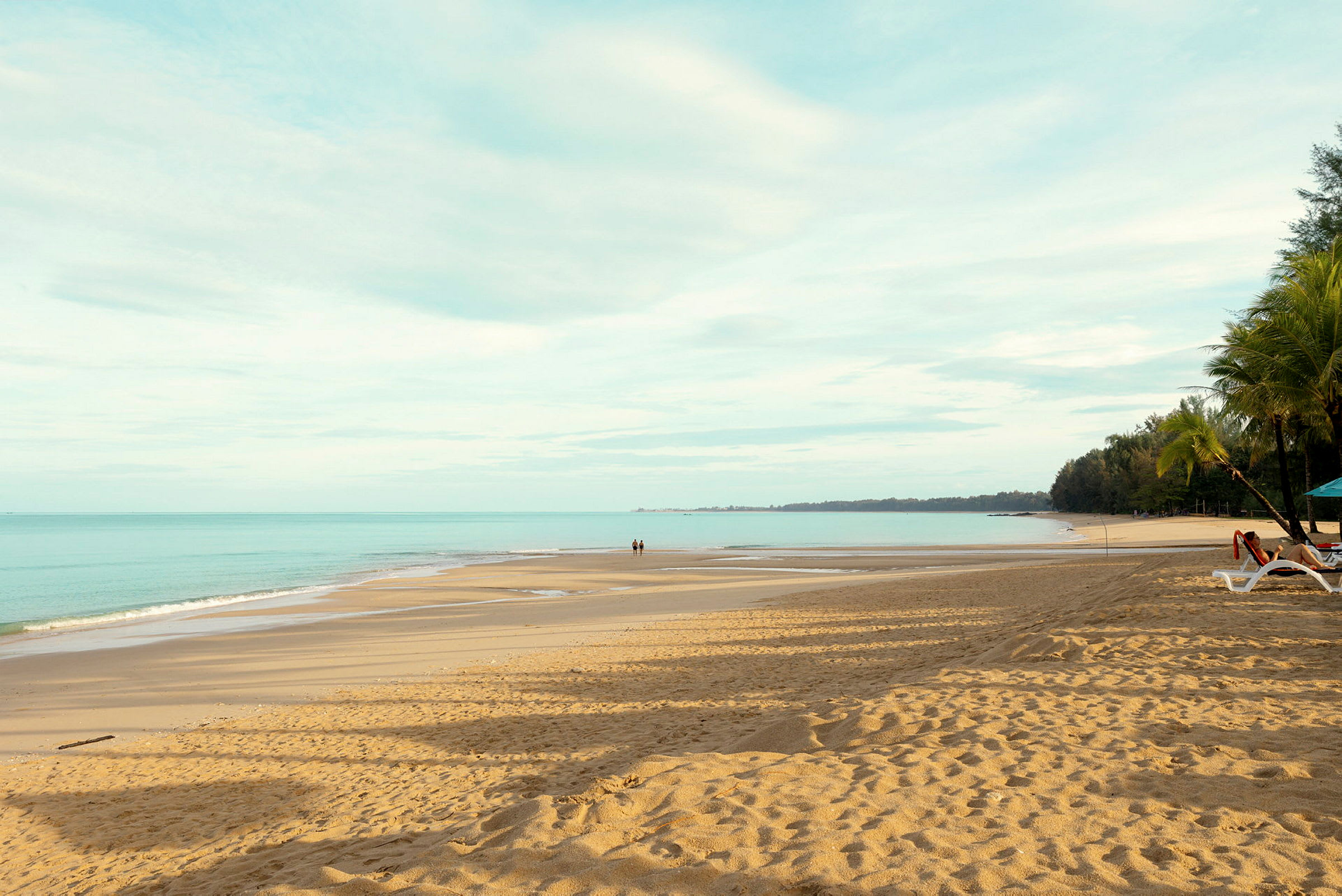 En sandstrand med utsikt över havet, två personer går på stranden. (AI-genererad text)