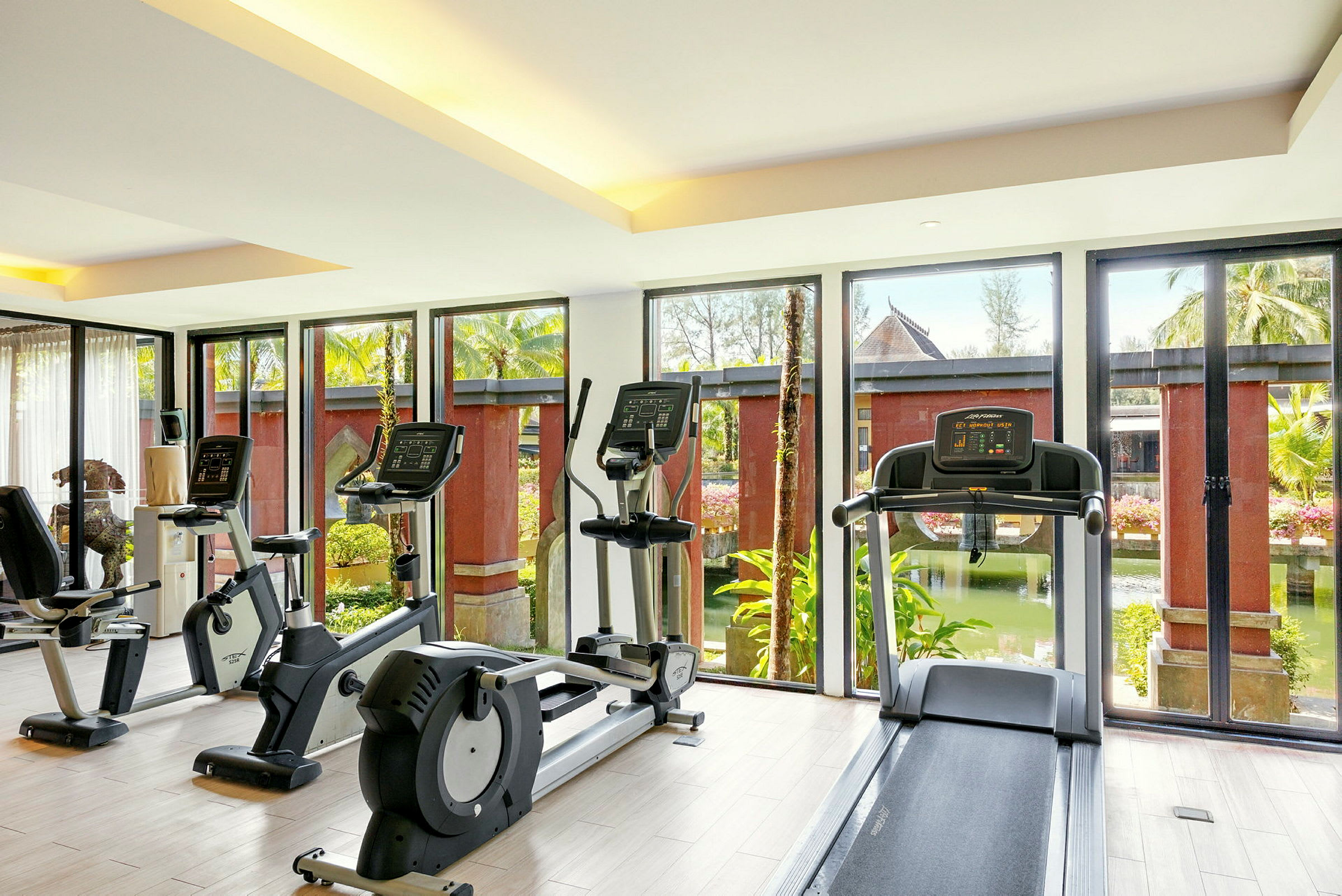 Ett gym med träningsmaskiner framför stora fönster som vetter mot en trädgård. (AI-genererad text)