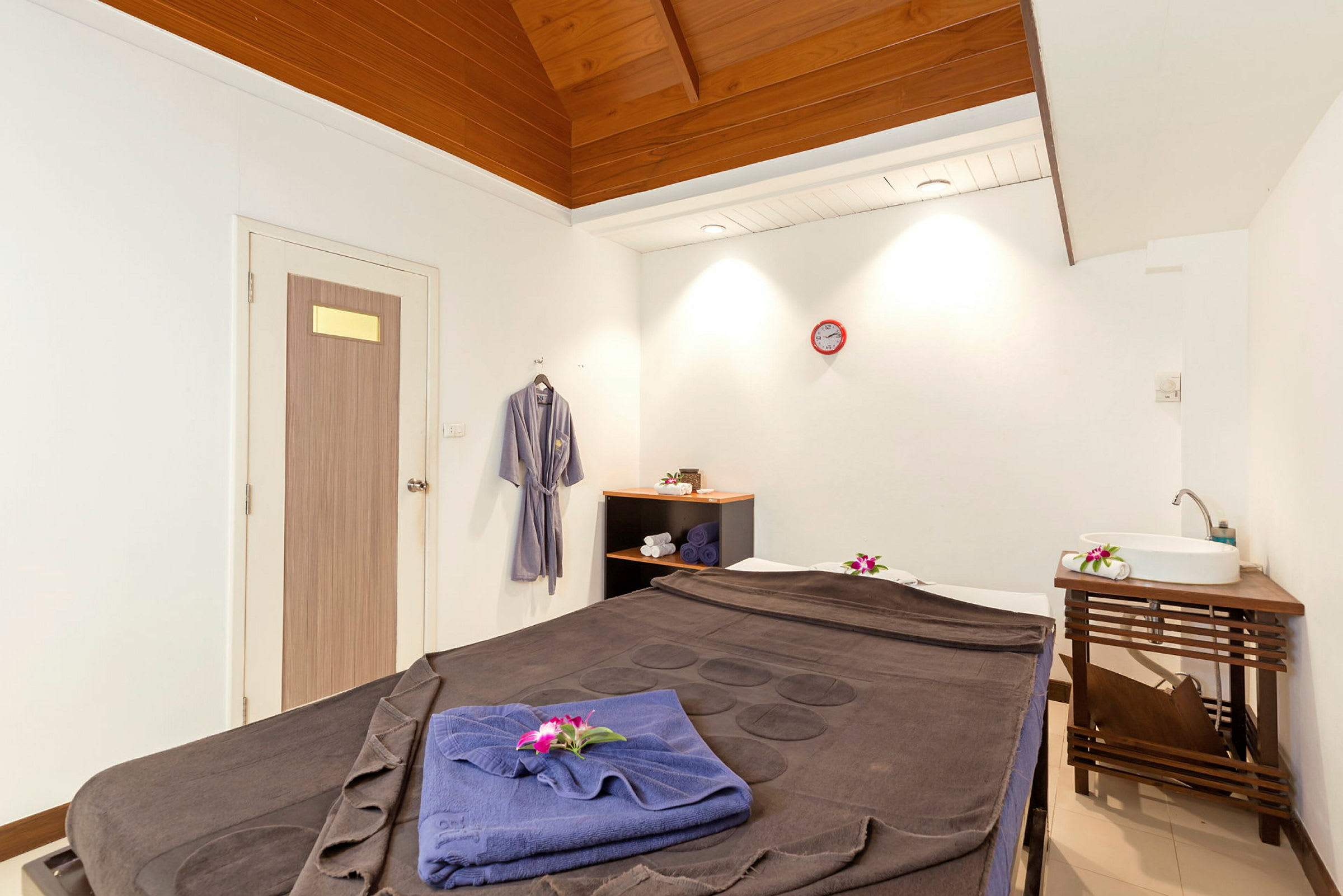 Ett behandlingsrum med massagebänk, handdukar och dekorativa blommor. (AI-genererad text)