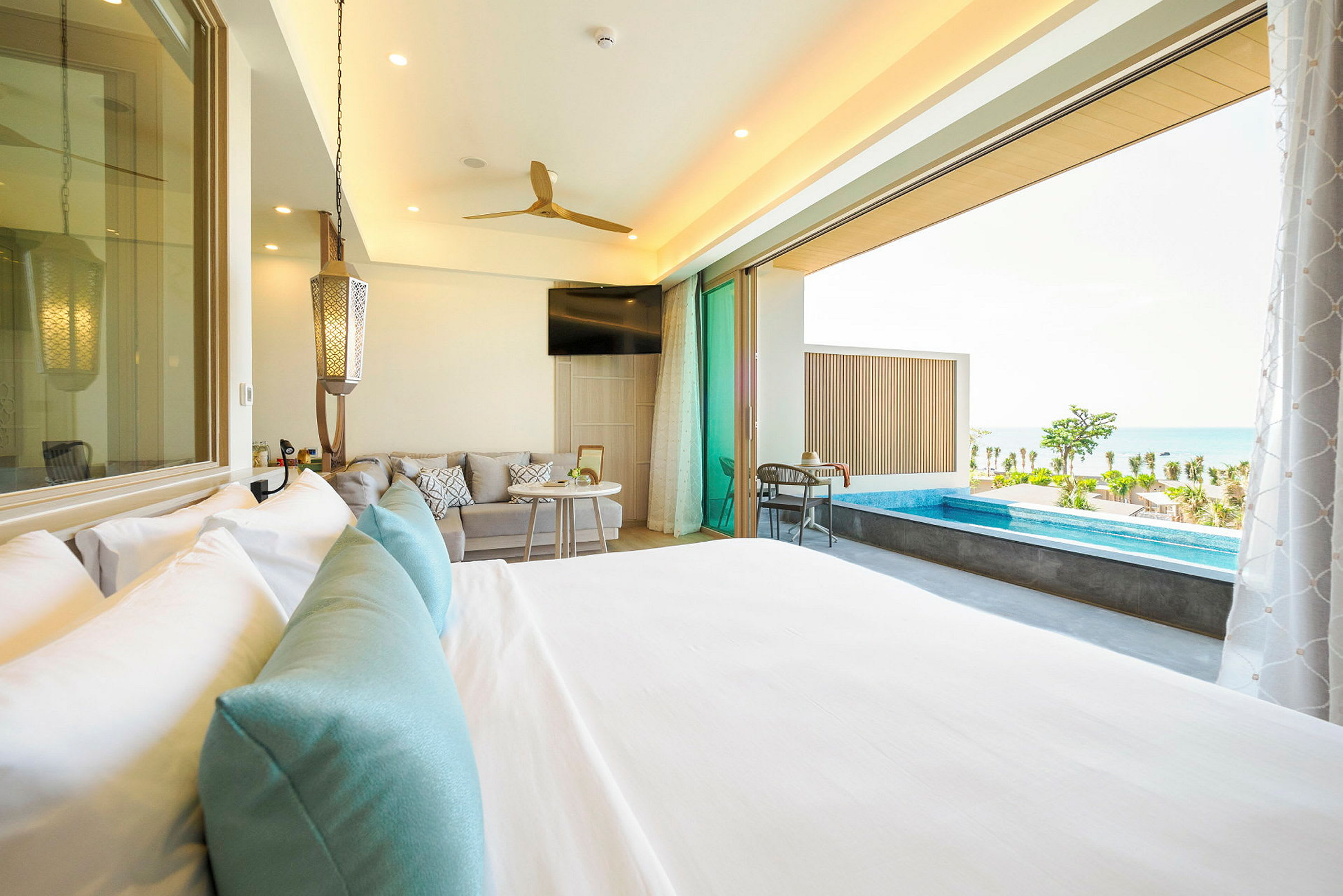 Hotellrum med säng, sittgrupp och utgång till terrass med liten pool och havsutsikt. (AI-genererad text)