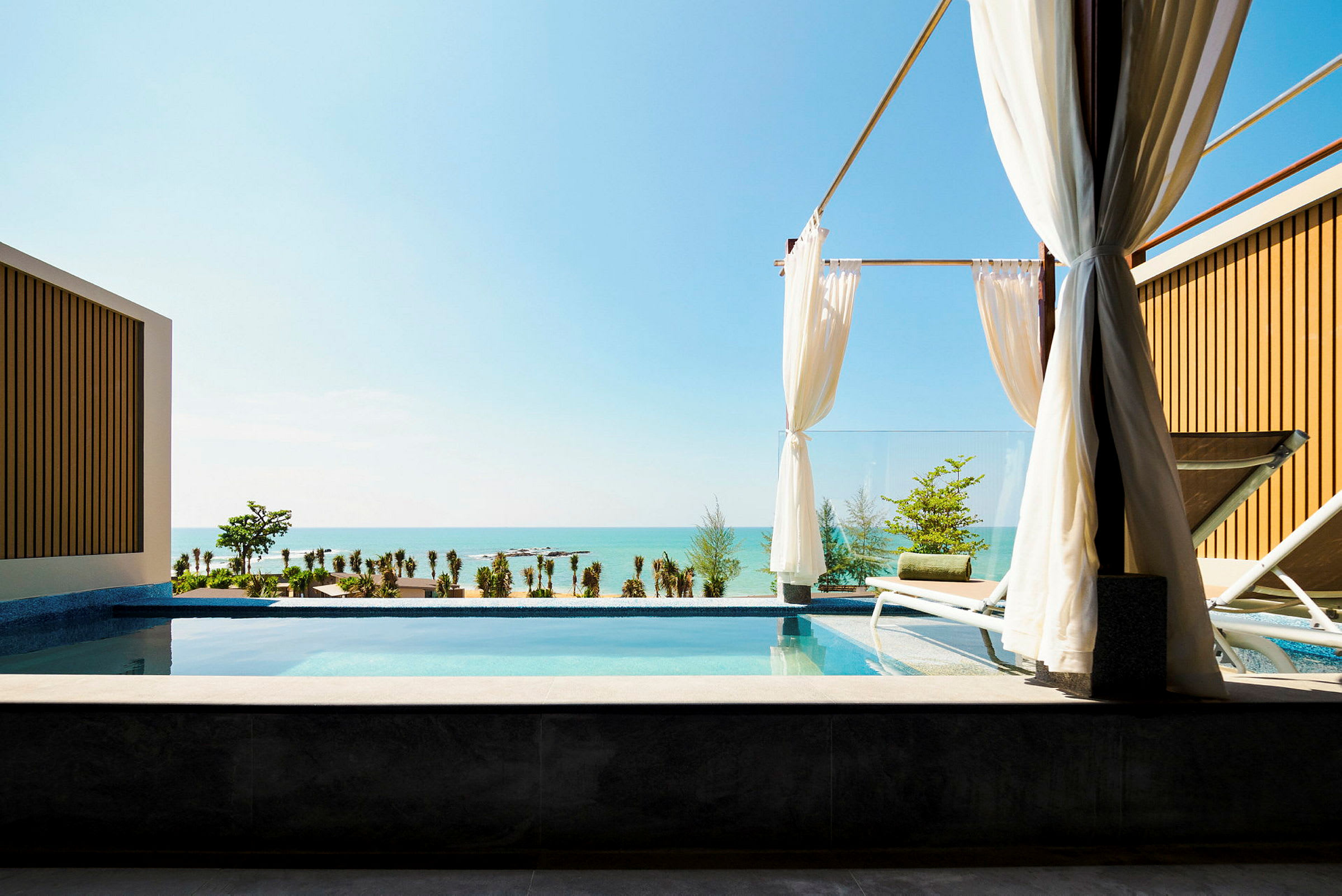 Utsikt från en pool med solstolar, gardiner och med havet i bakgrunden. (AI-genererad text)