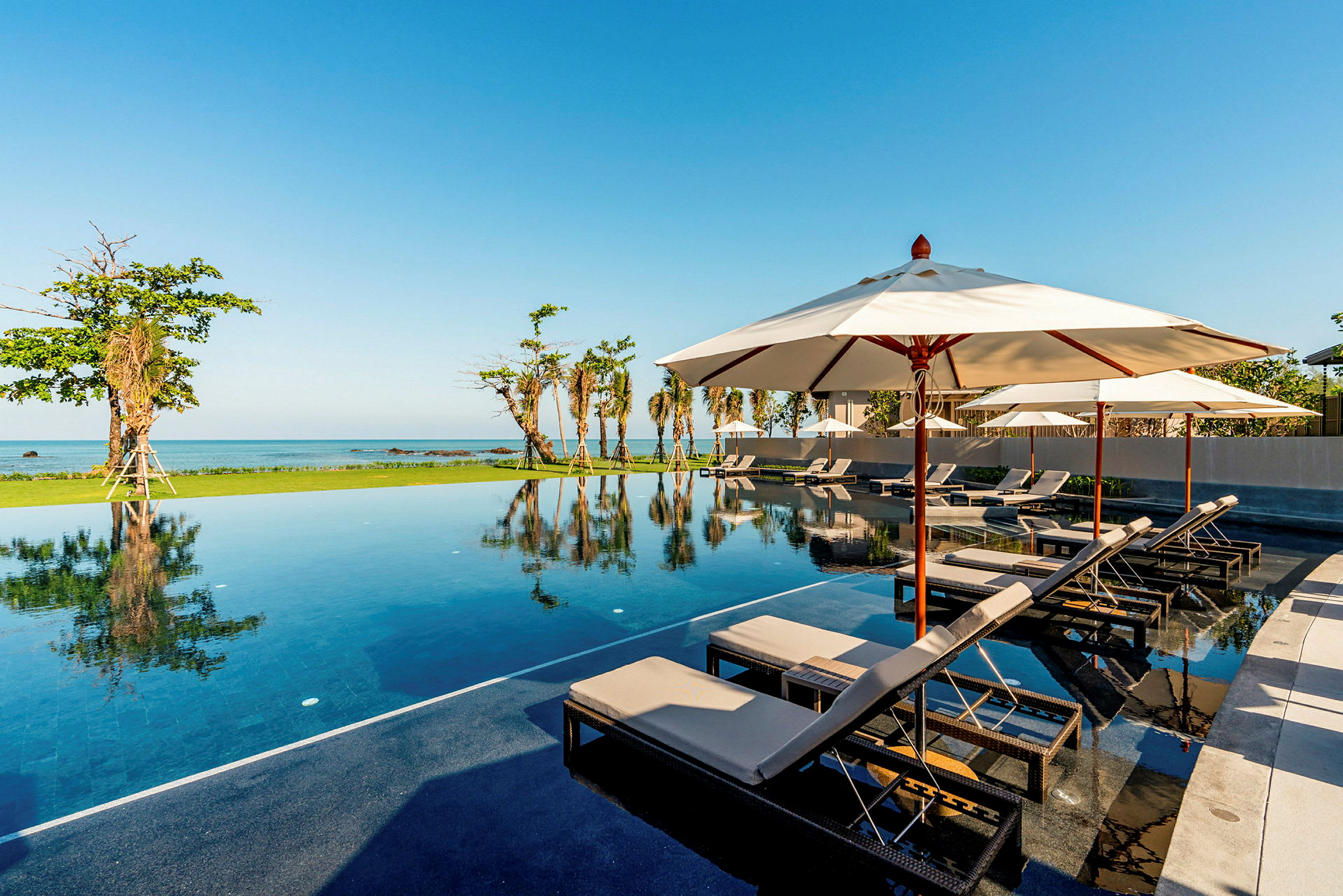 Pool med solstolar och parasoller vid havet. (AI-genererad text)