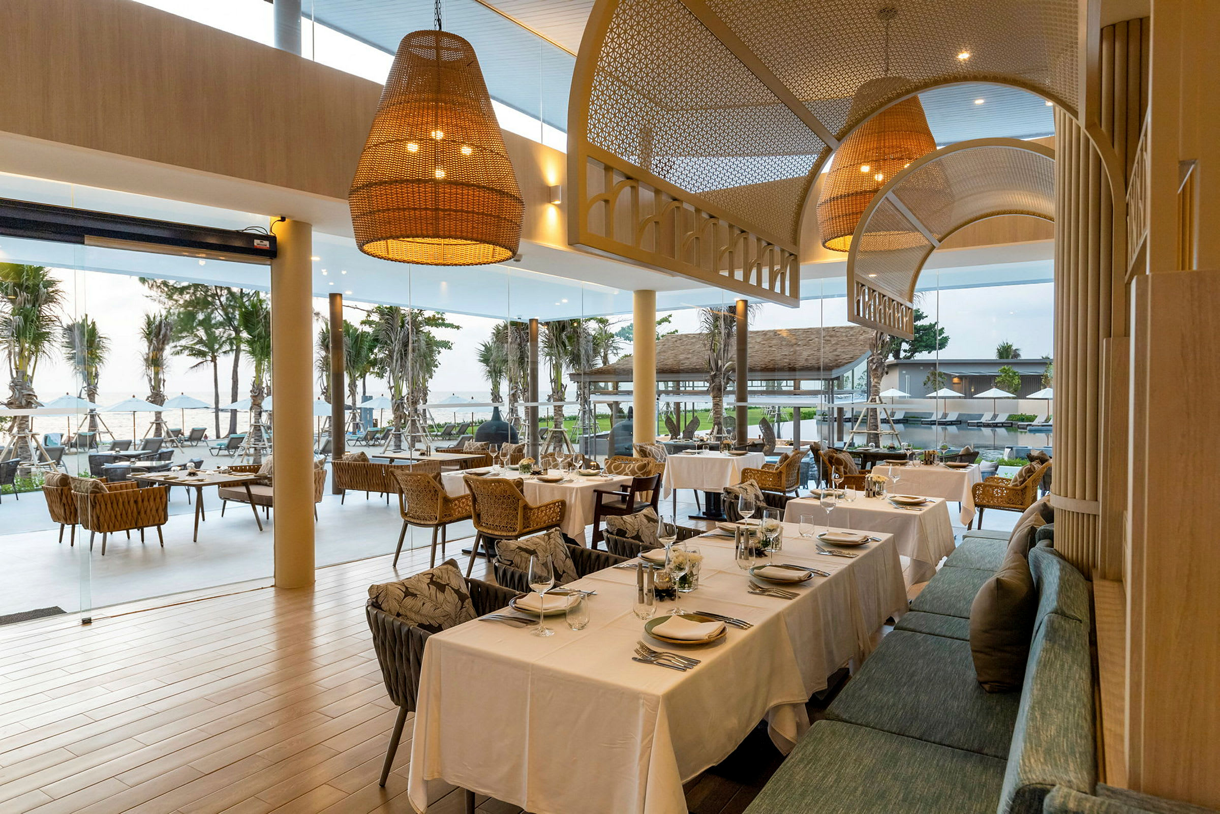 Restaurang med dukade bord och utsikt över palmträd och hav genom stora fönster. (AI-genererad text)