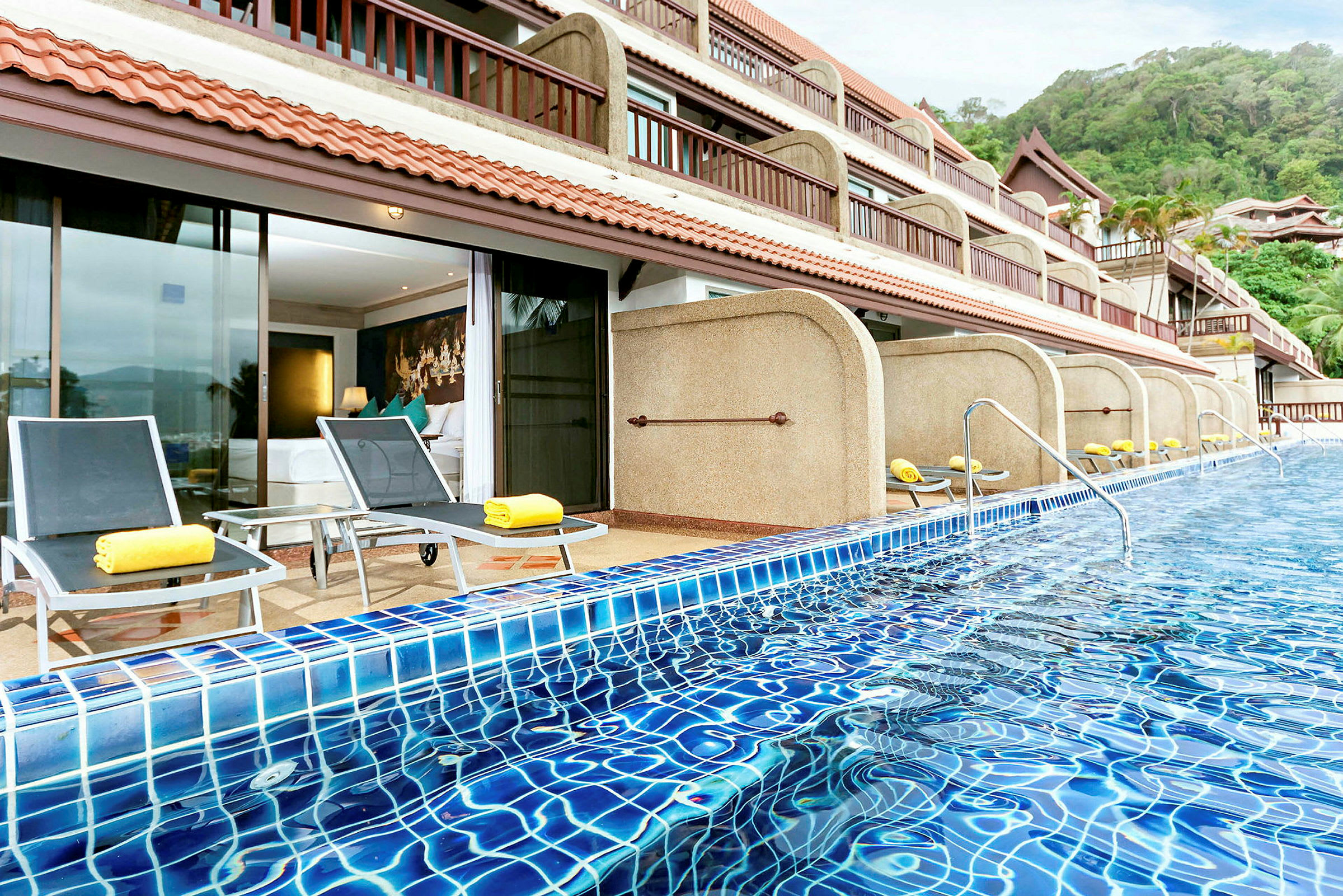 En bild på en pool framför ett hotell med solstolar och terrasser. (AI-genererad text)