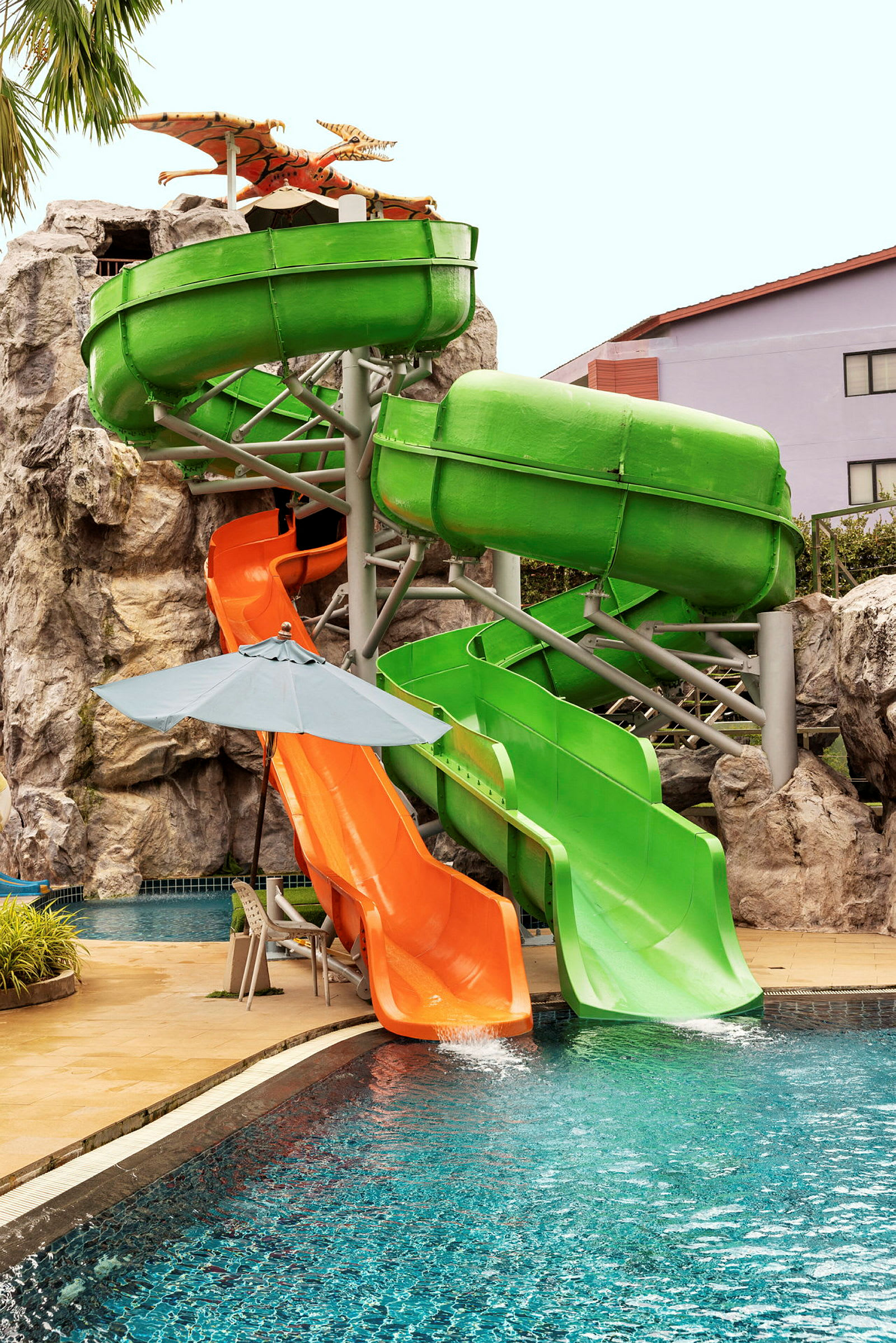 Två vattenrutschbanor, en grön och en orange, som leder ner i en swimmingpool. (AI-genererad text)