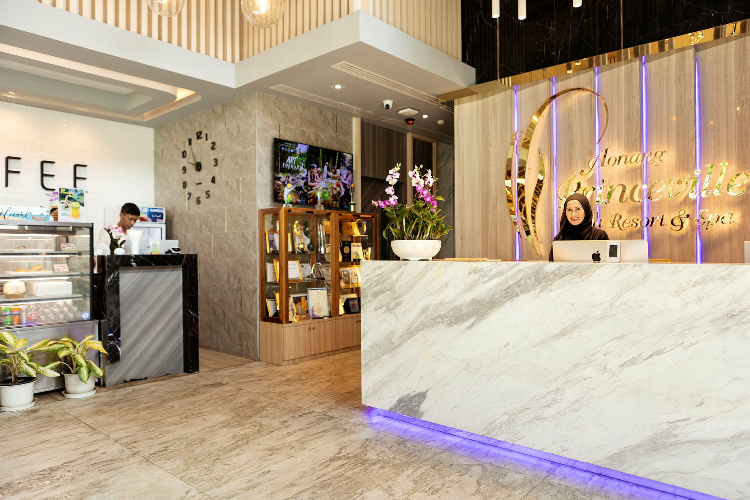 Reception med marmordisk och skylt med texten "Ao Nang Princeville Resort & Spa". En person står bakom disken. Till vänster syns en liten kafédisk och ett vitrinskåp med priser. (AI-genererad text)