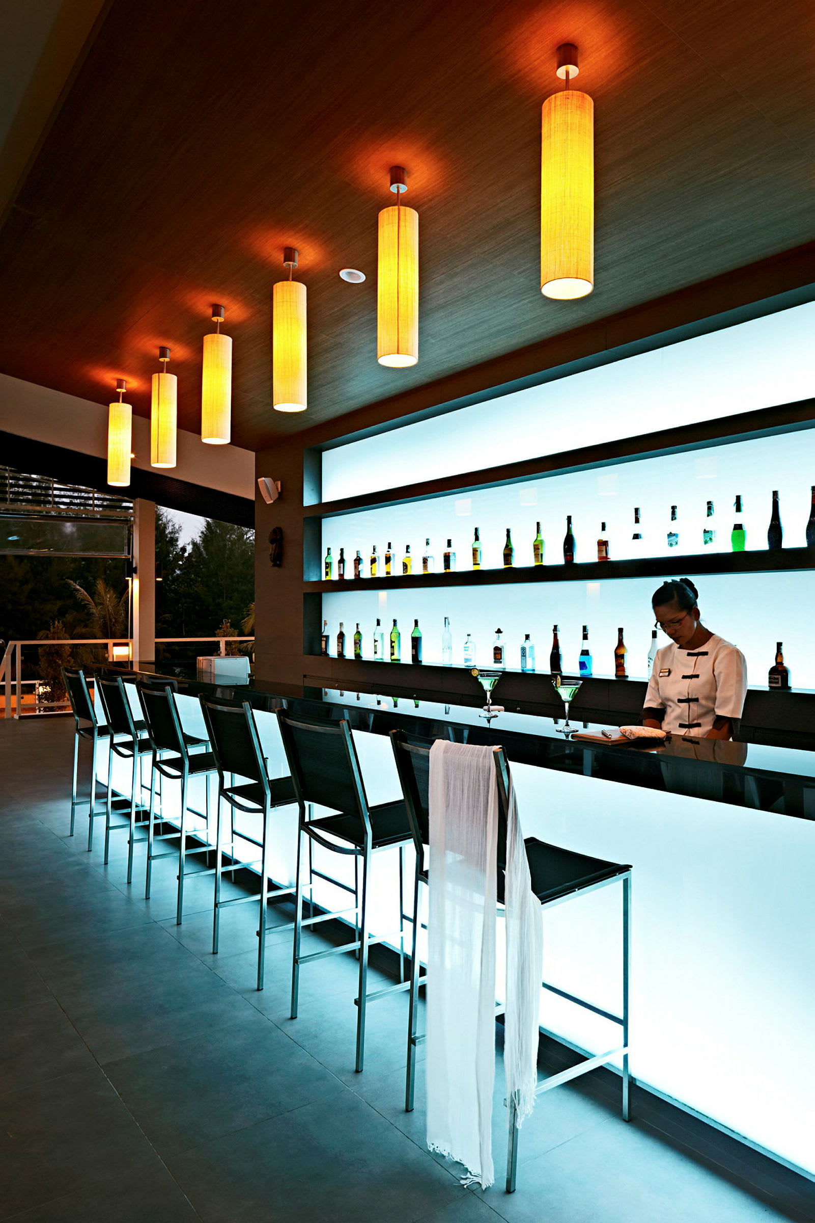 Modern bar med rad av höga stolar och belyst bakvägg med flaskor. (AI-genererad text)