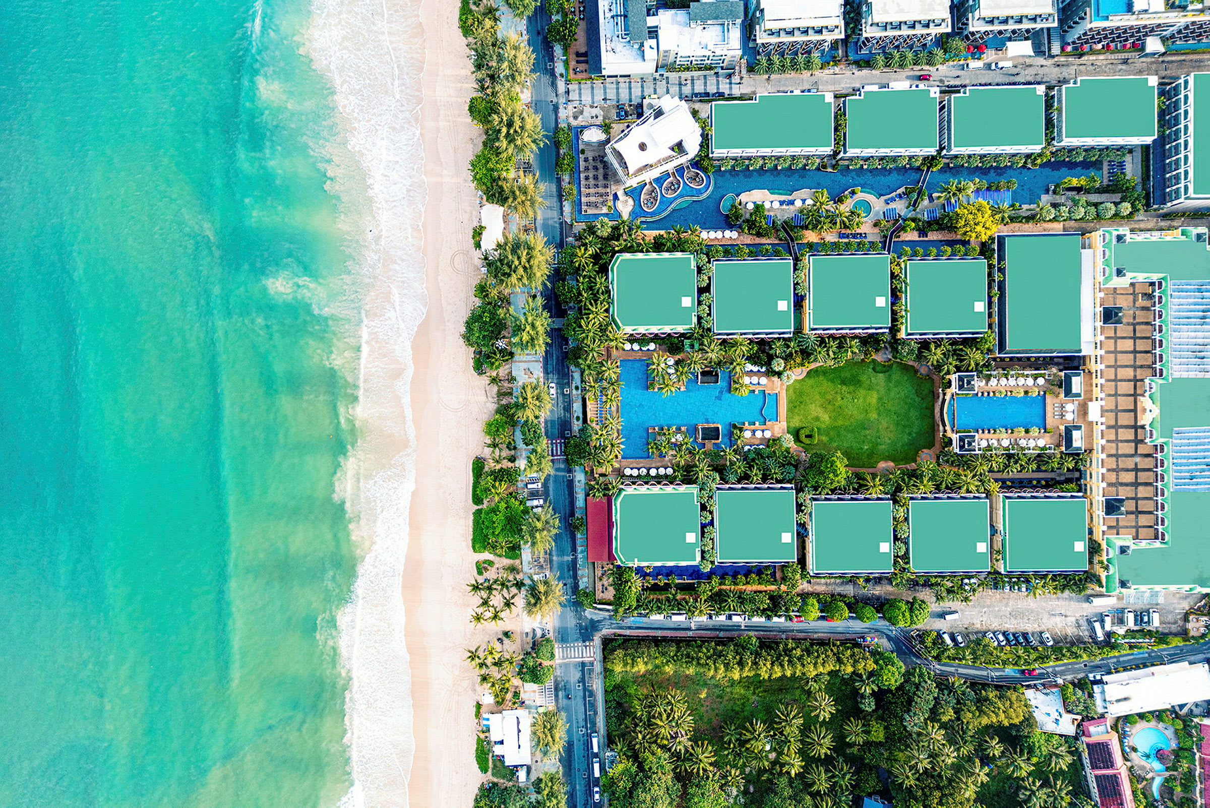 Flygbild som visar en strand med grönt klart vatten och ett hotellkomplex med grönområden och bassänger. (AI-genererad text)