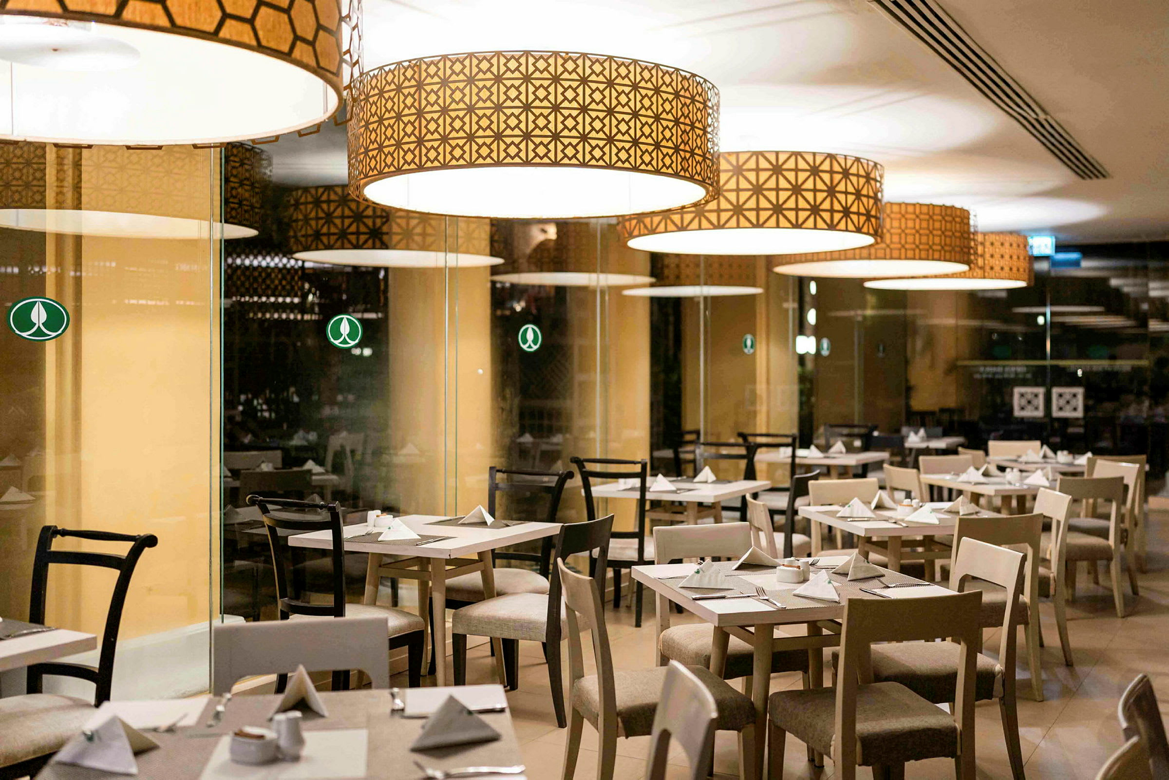 Bild av en restaurang med flera dukade bord och stolar under stora dekorativa lampor. (AI-genererad text)