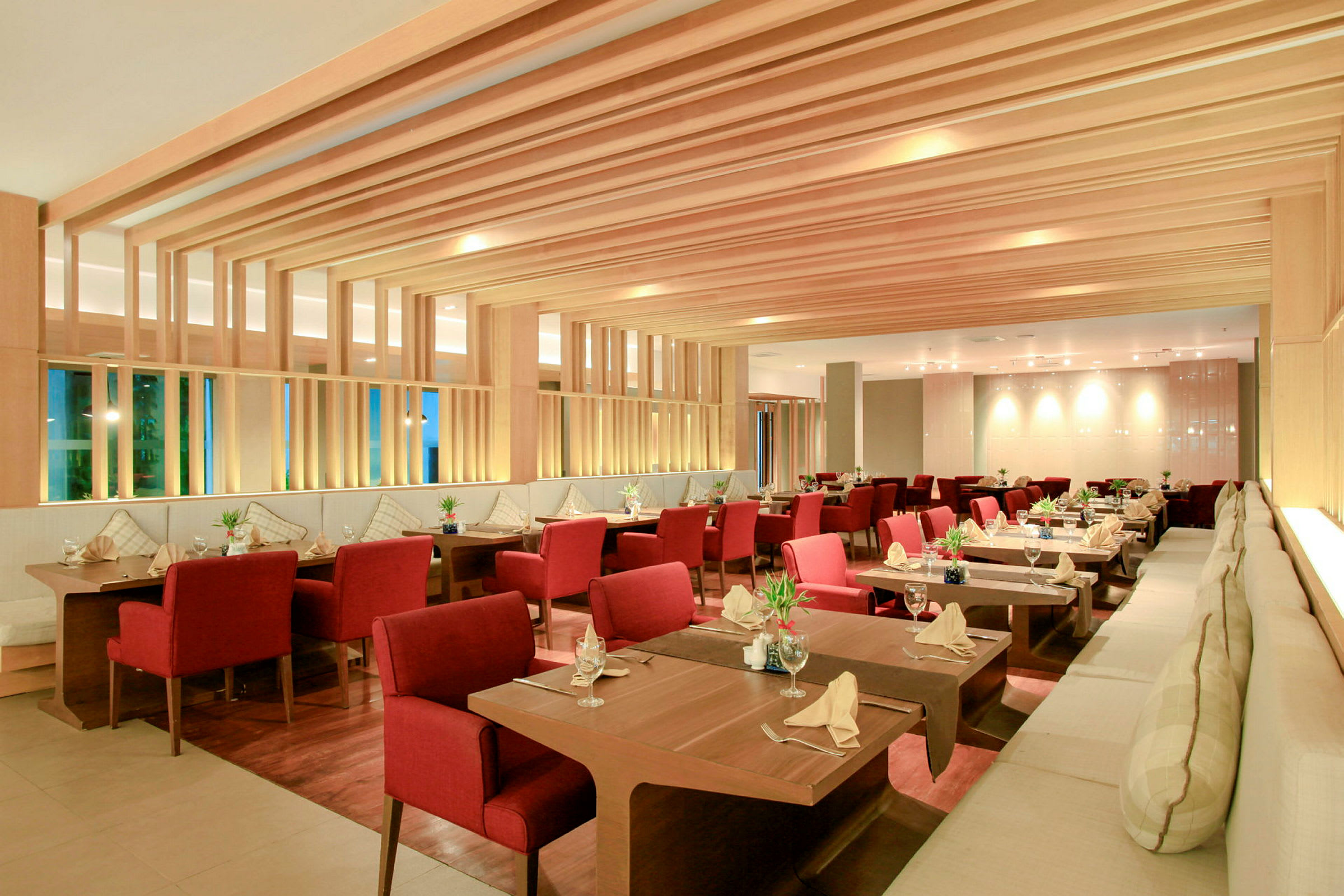 En stilren restaurang interiör med bord och röda sittplatser, trädetaljer och elegant dukning. (AI-genererad text)