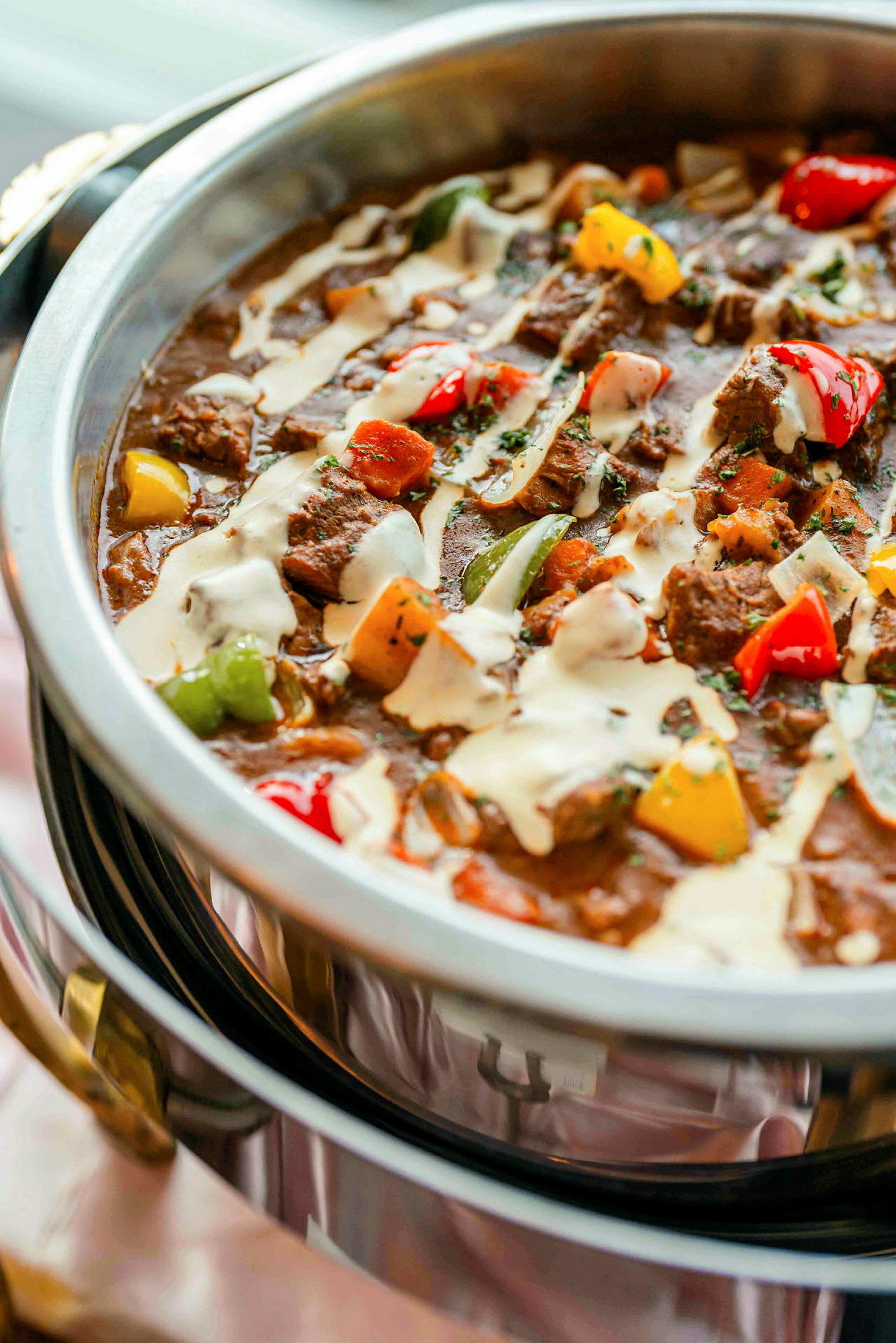 En gryta med kött och grönsaker toppad med sås, serverad i en metallskål. (AI-genererad text)
