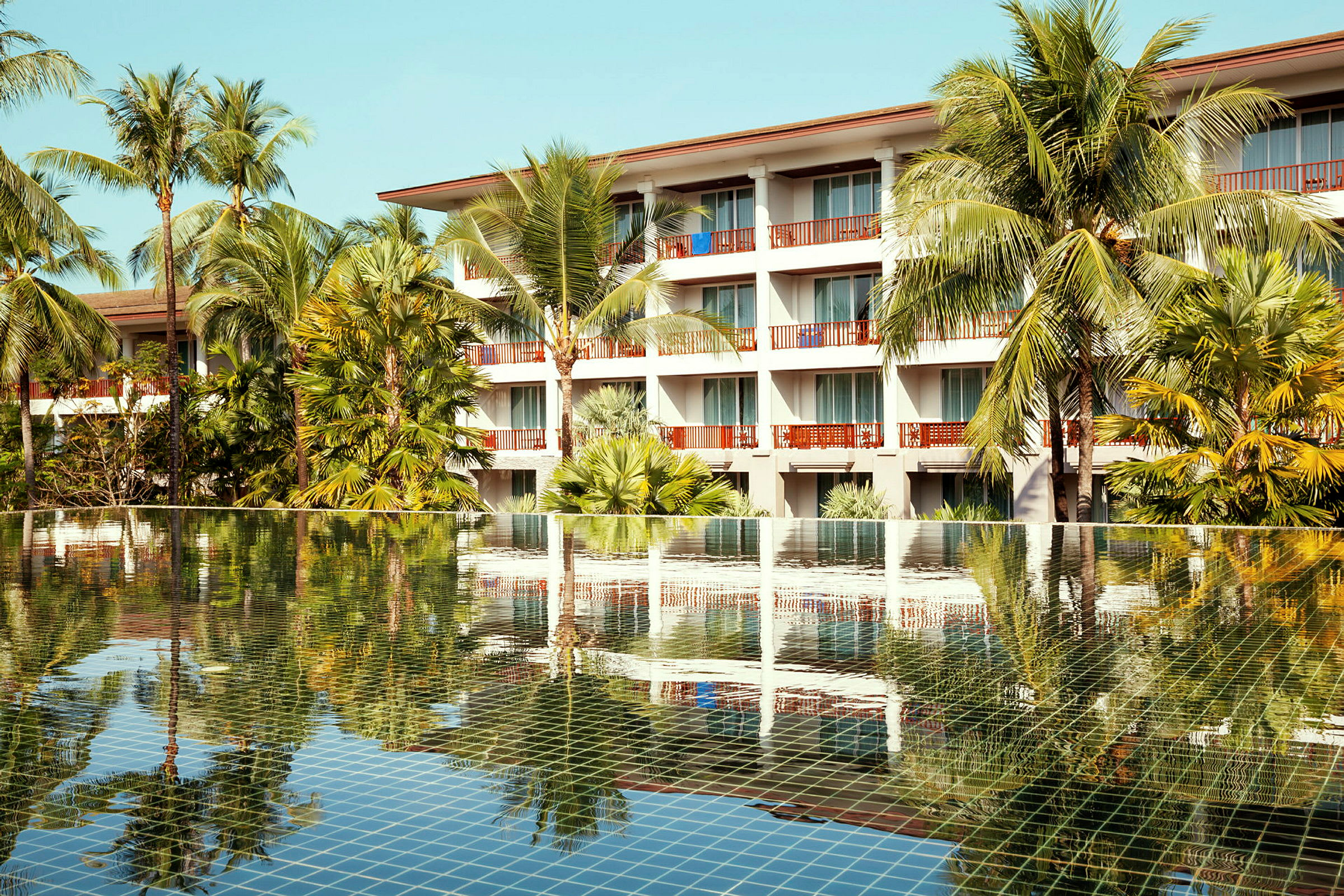 Hotellbyggnad bakom en pool med palmträd. (AI-genererad text)