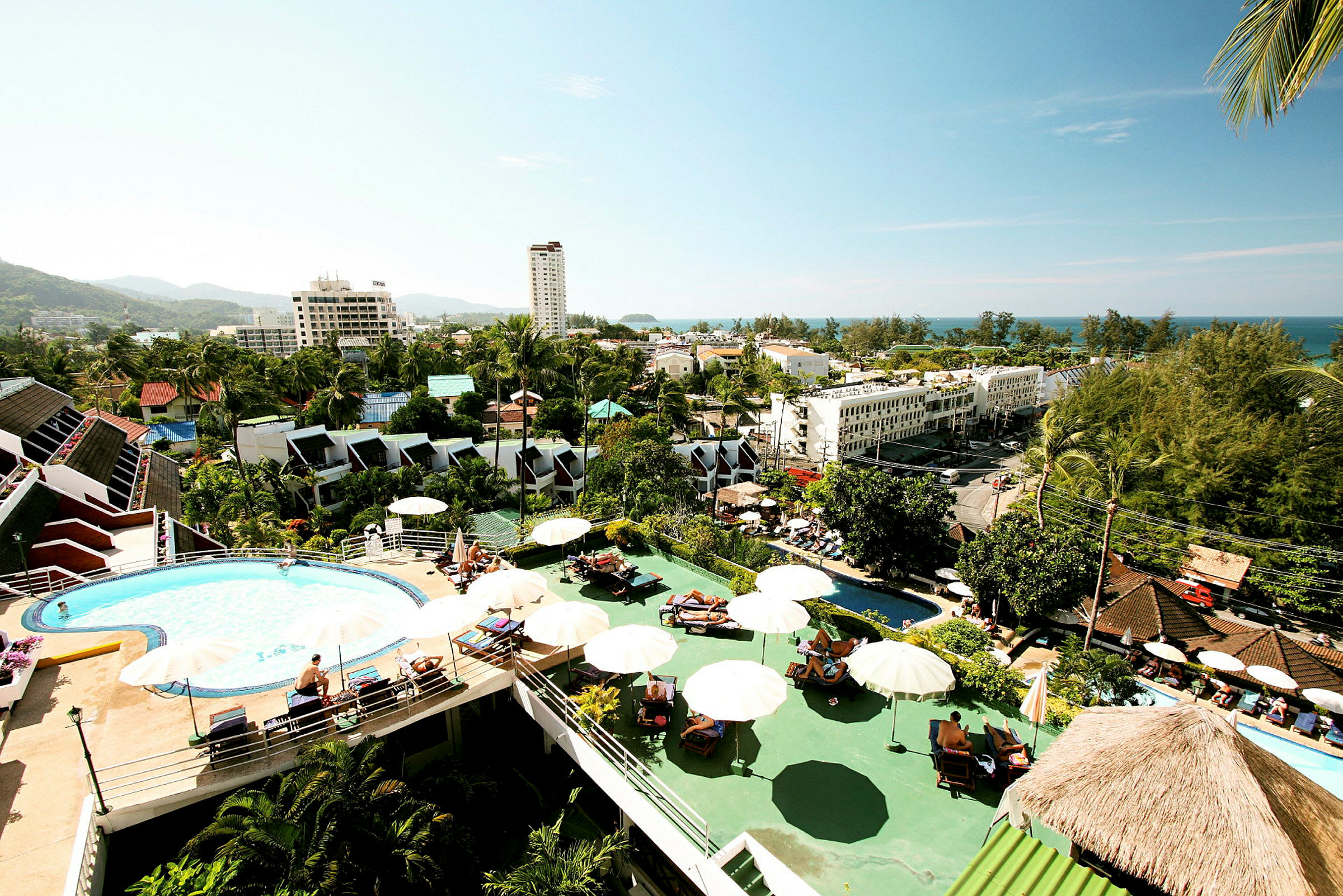 Vy över hotellområde med pool, parasoller och byggnader i tropisk miljö. (AI-genererad text)