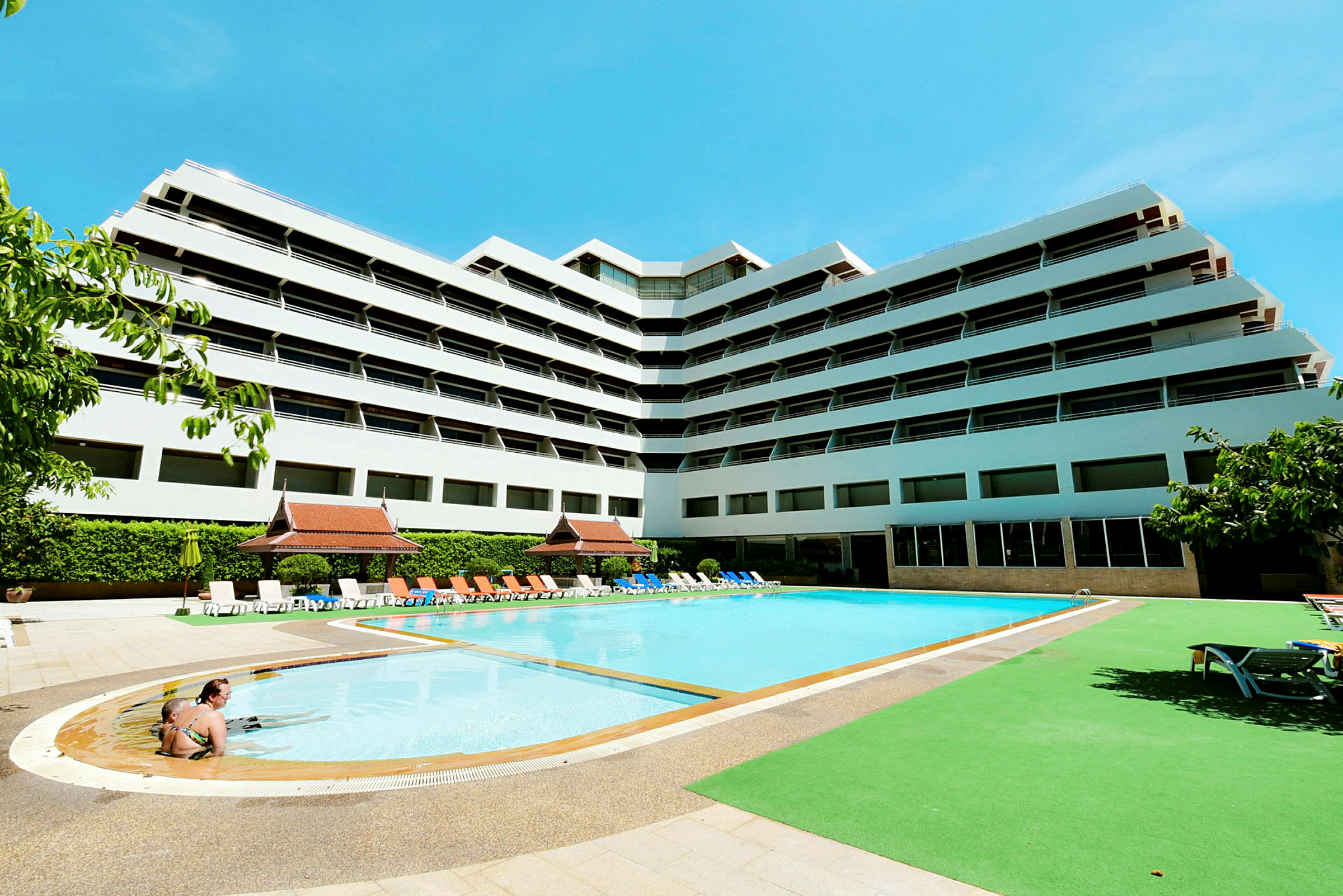 Modern hotellbyggnad med pool och solstolar utanför. (AI-genererad text)