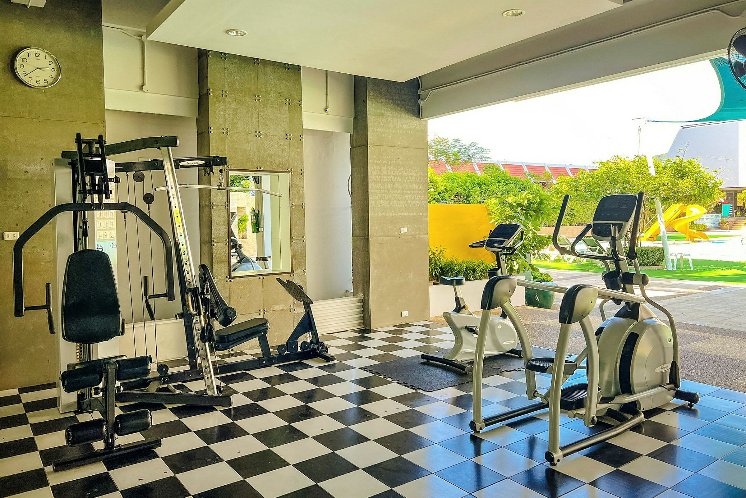 Ett gym med olika träningsmaskiner. Utanför är en grönskande trädgård med rutschkana. (AI-genererad text)