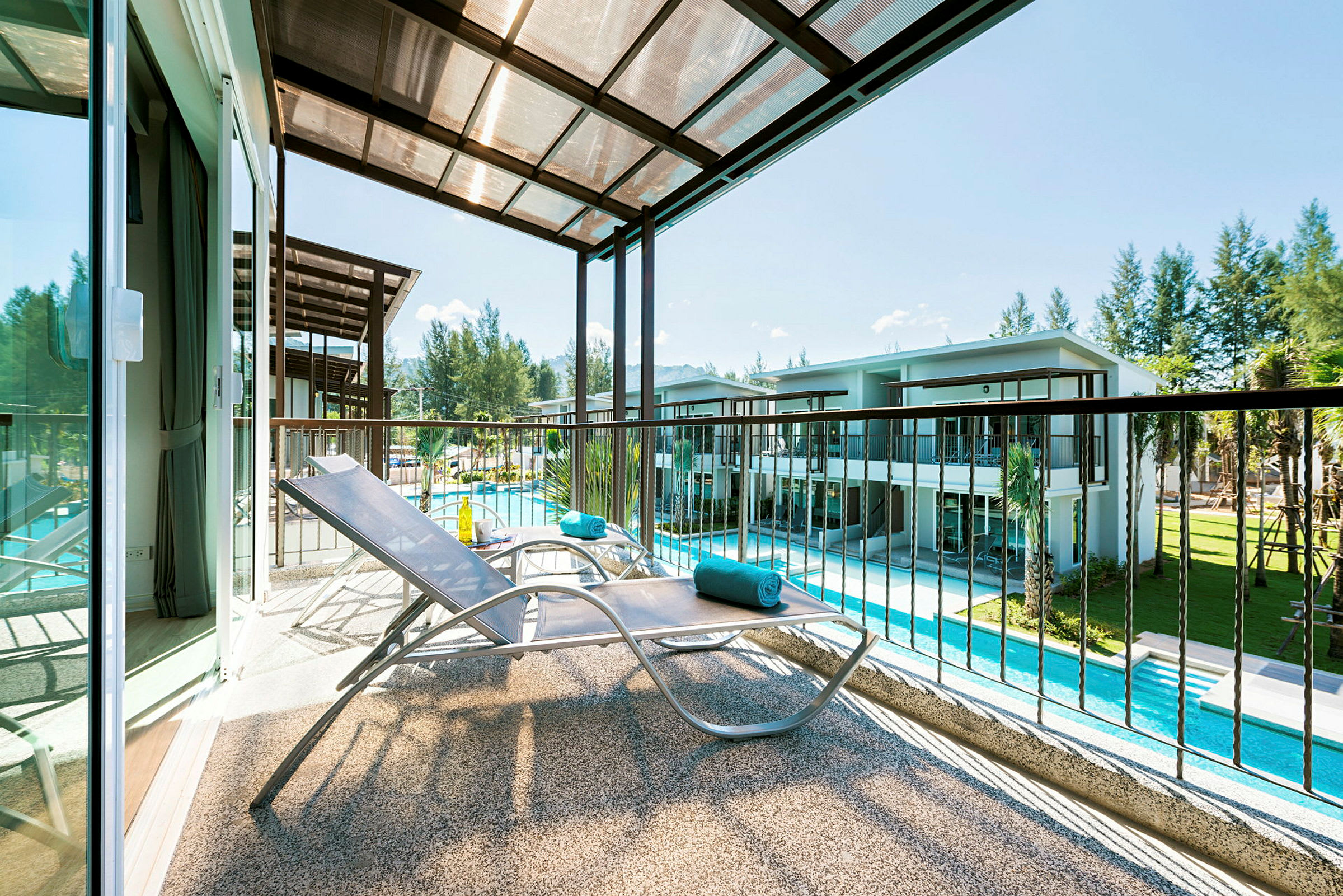 En balkong med en solstol och utsikt över en swimmingpool och grönska. (AI-genererad text)