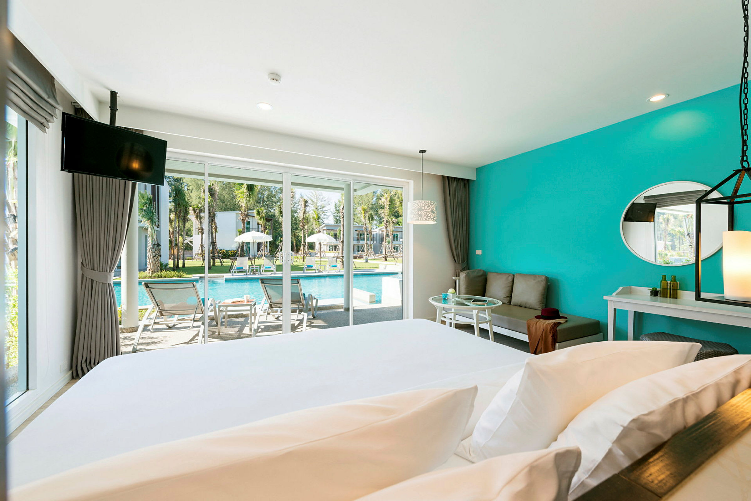Hotellrum med säng och sittgrupp, stora fönster med utsikt mot poolområdet. (AI-genererad text)