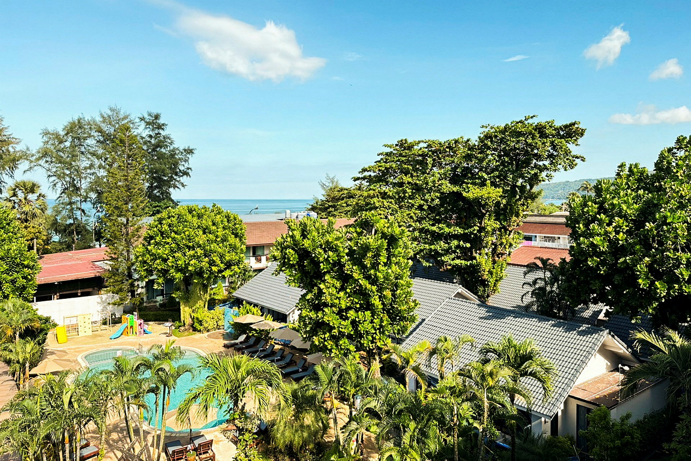 Utsikt över hotellområde med pool och grönska, i bakgrunden syns havet. (AI-genererad text)