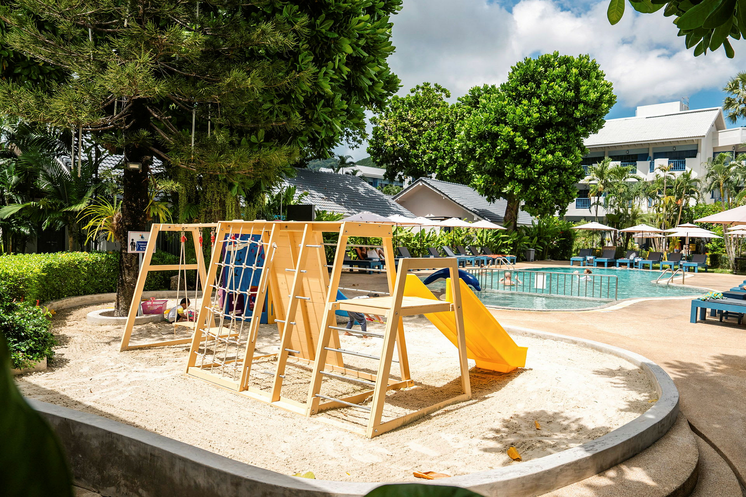 Lekplats med klätterställning och rutschkana nära en pool. (AI-genererad text)