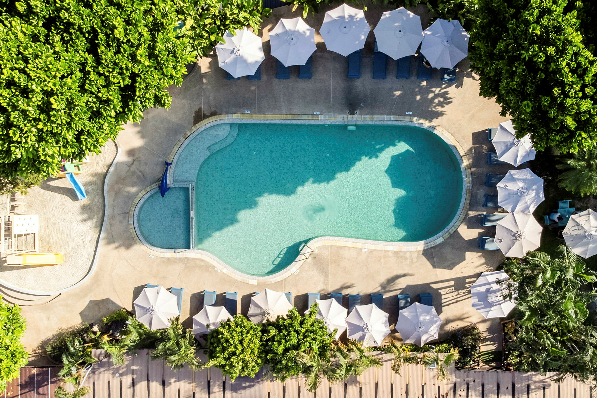 En oval pool omgiven av solstolar och parasoller samt grönska. (AI-genererad text)
