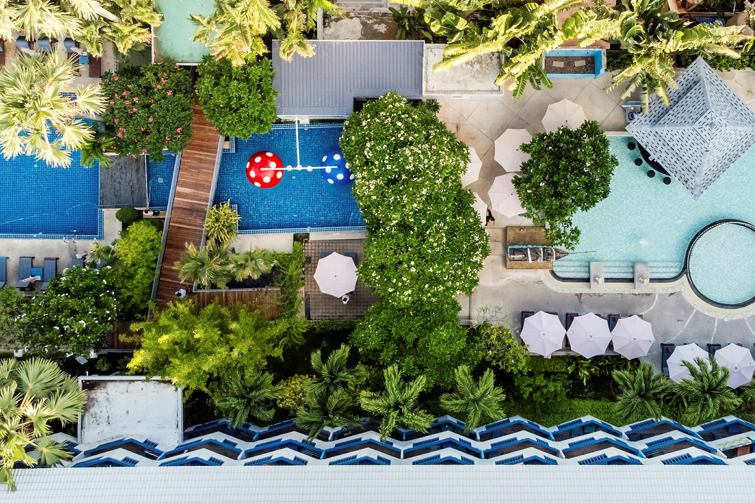 Flygbild av ett hotellområde med pooler, grönska och parasoller. (AI-genererad text)