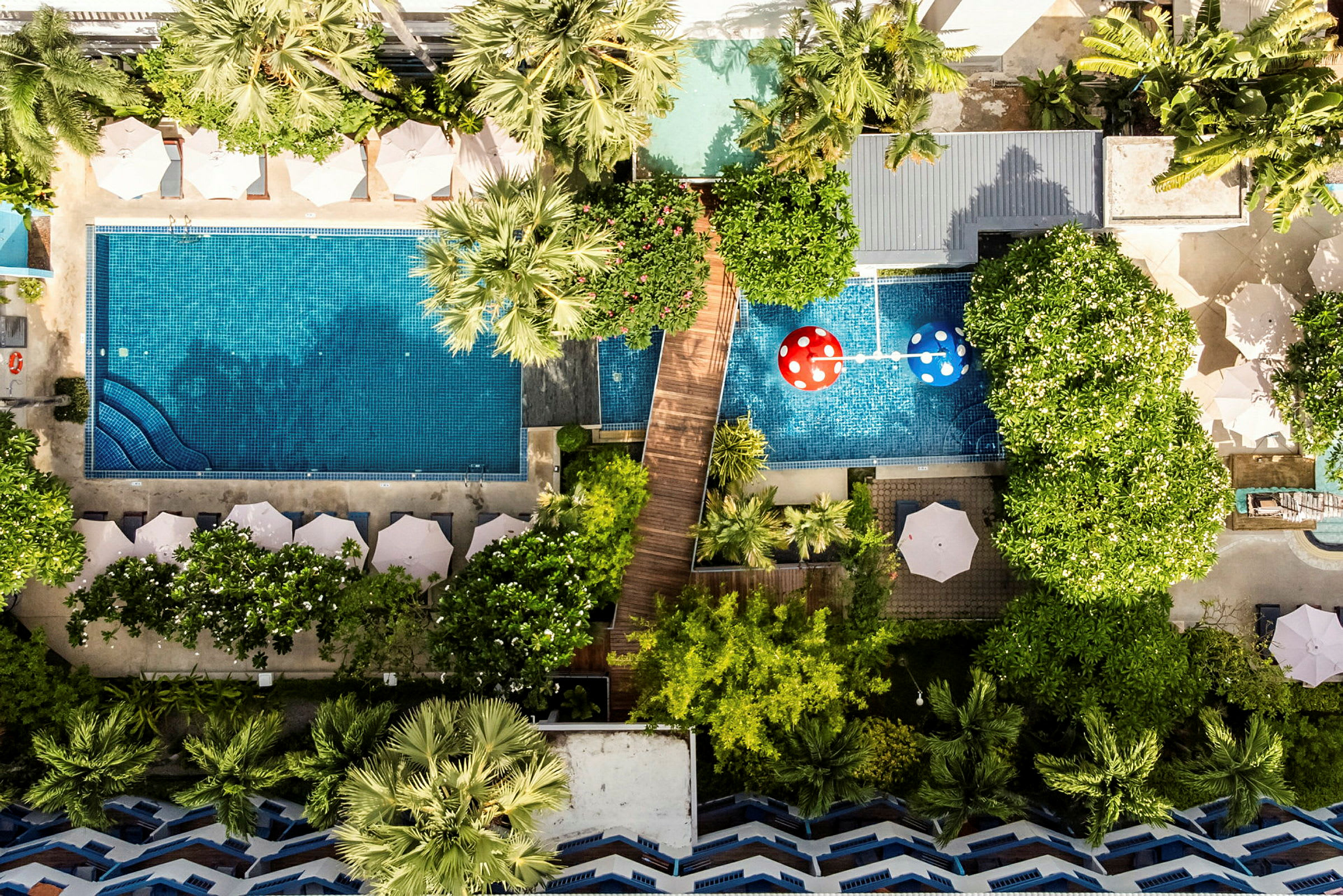 Flygfoto av en hotellpool omgiven av solstolar, parasoller och grönskande träd. (AI-genererad text)