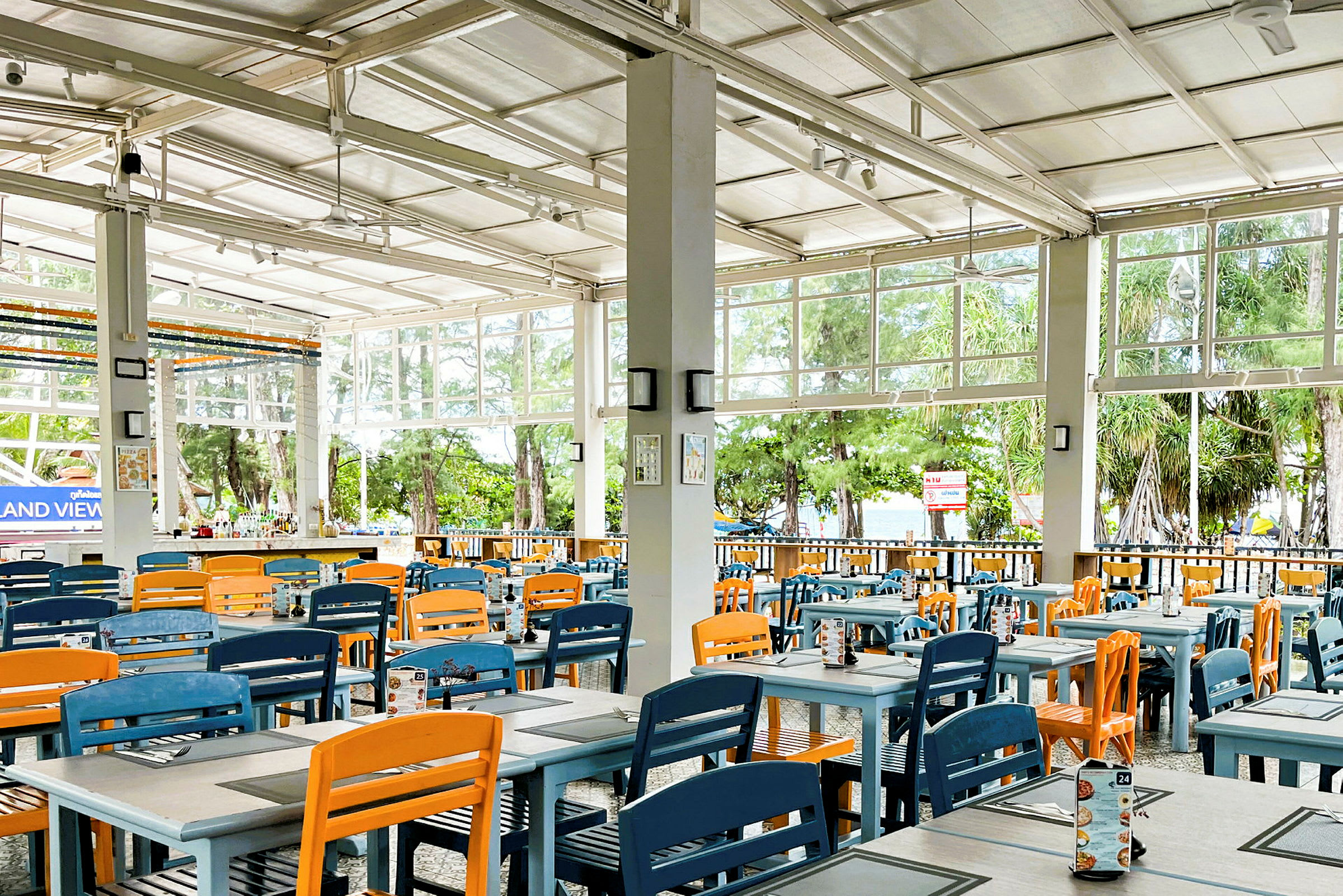 Restaurang med färgglada stolar och öppet till en grönskande utsikt. (AI-genererad text)