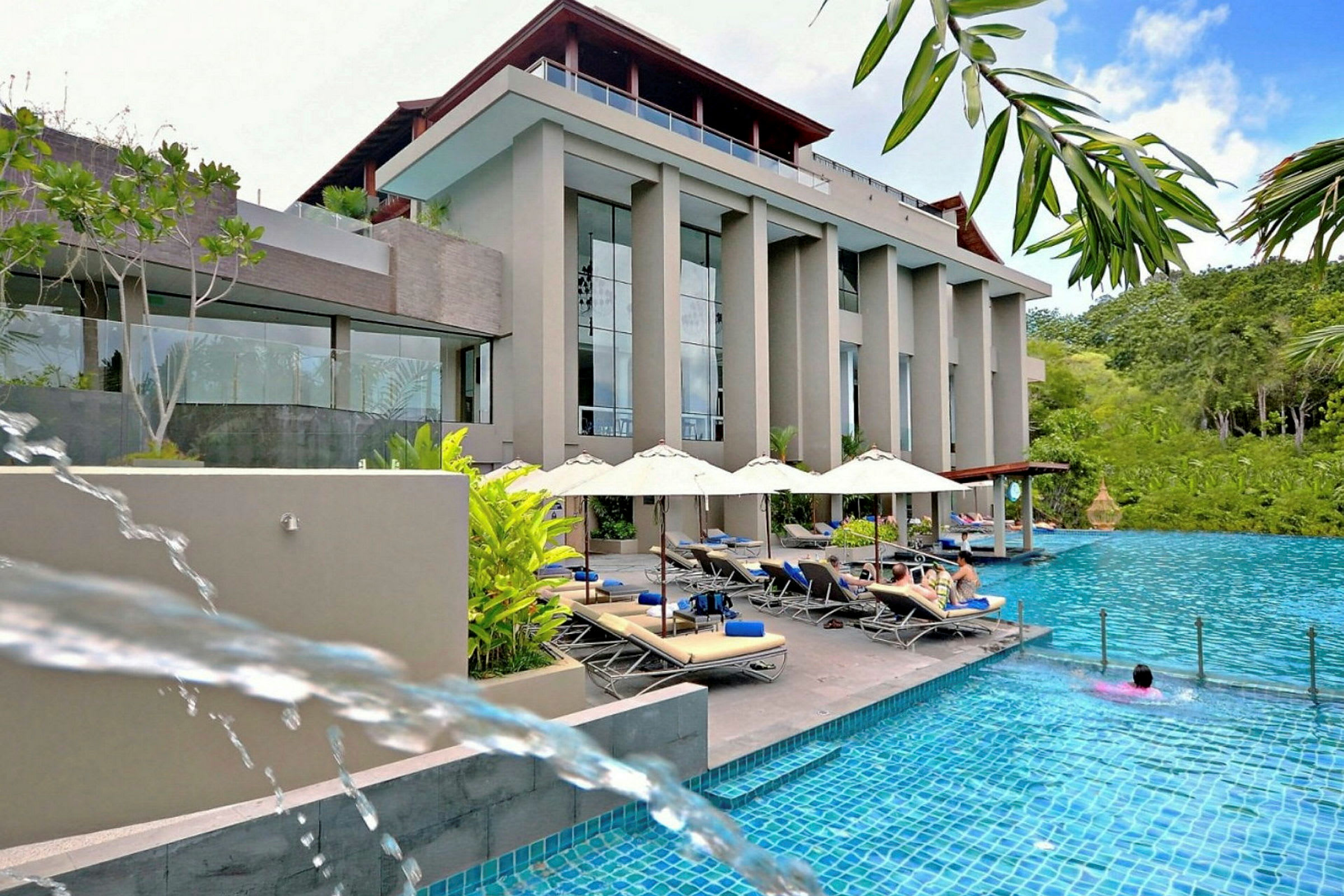 Bild av en hotellfasad vid en pool med solstolar och parasoller. (AI-genererad text)
