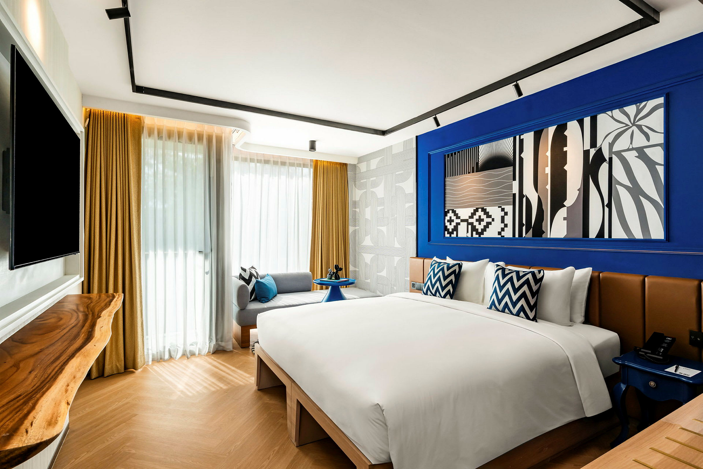 Ett modernt hotellrum med en dubbelsäng, dekorationer i blått och vitt, samt stora fönster med gardiner. (AI-genererad text)