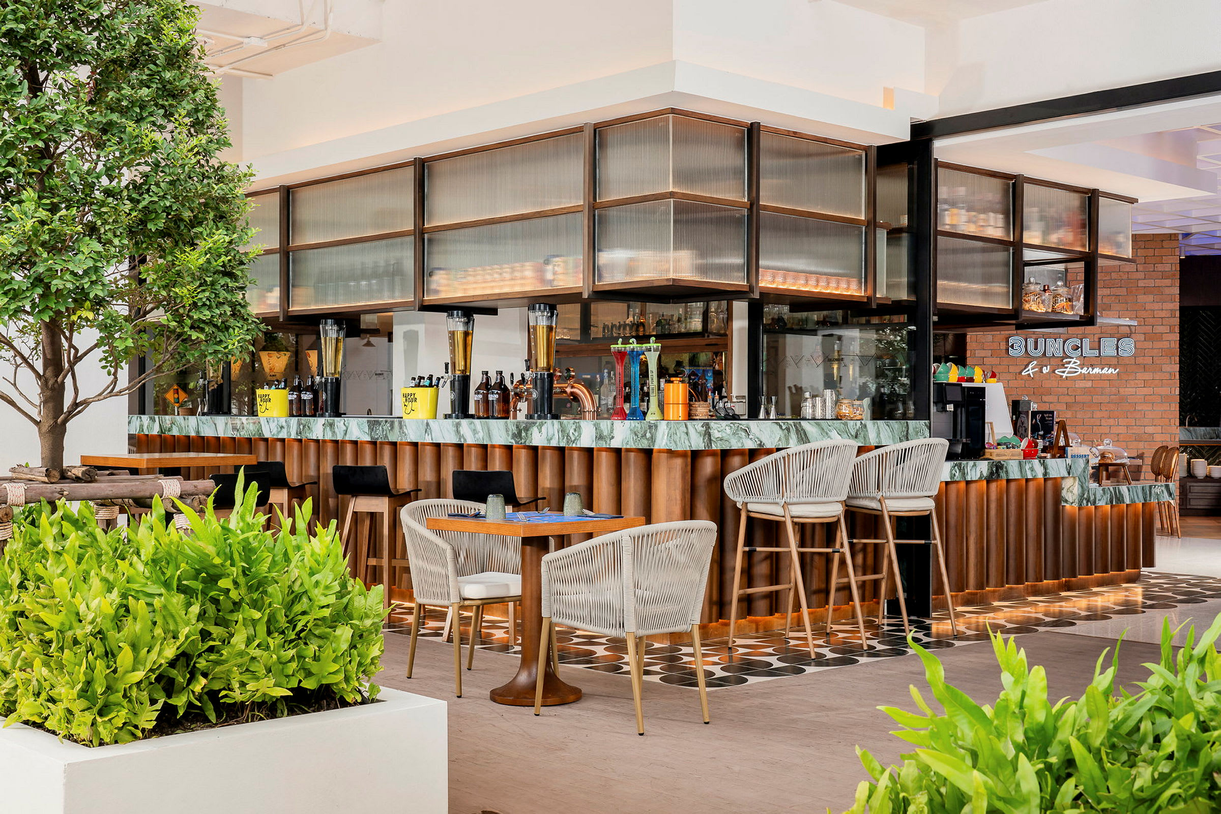 En modern bar med trä- och marmordetaljer, omgiven av gröna växter och sittplatser med stolar och bord. (AI-genererad text)