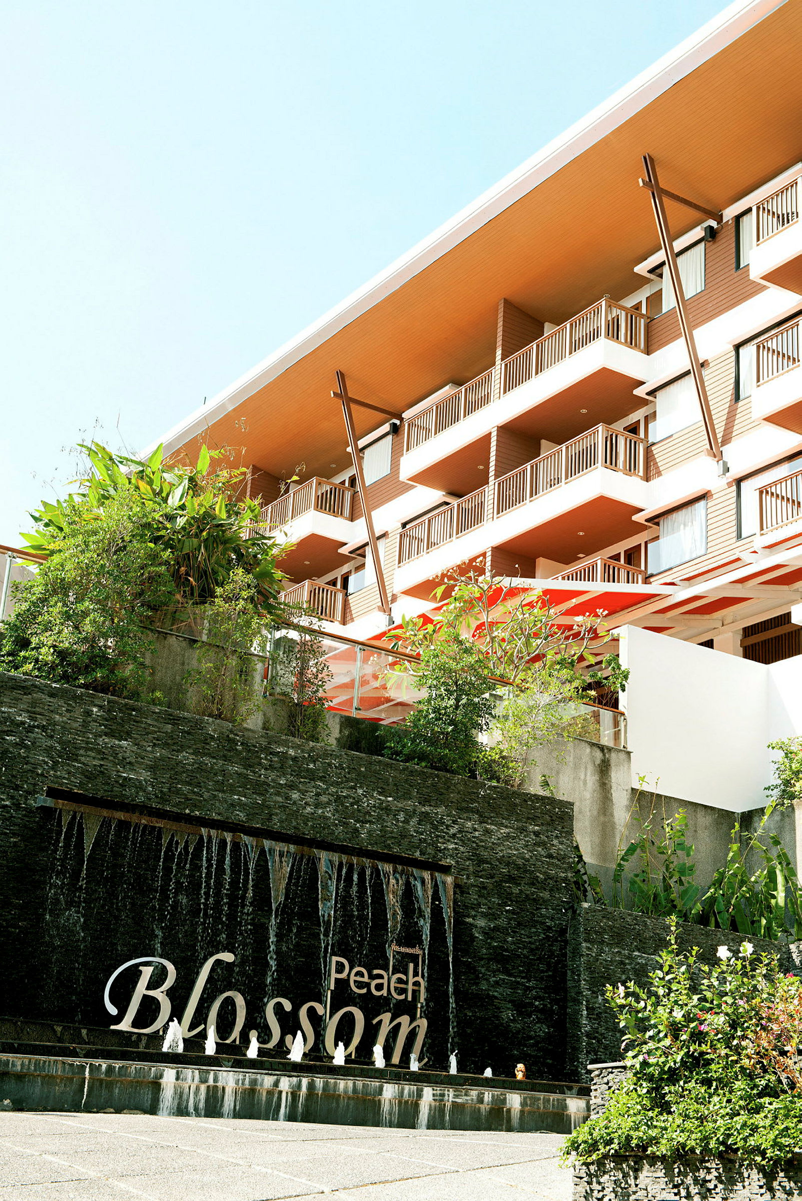 Ett hotell med moderna balkonger, grönska och en vattenfontän med texten "Peach Blossom". (AI-genererad text)