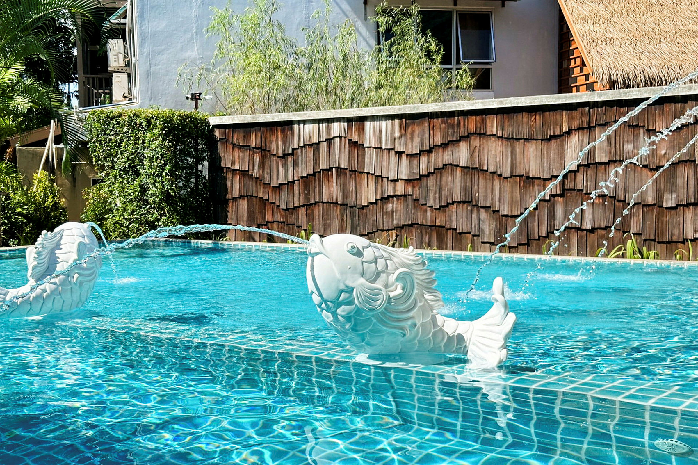 Vita skulpturer av fiskar sprutande vatten i en pool. (AI-genererad text)