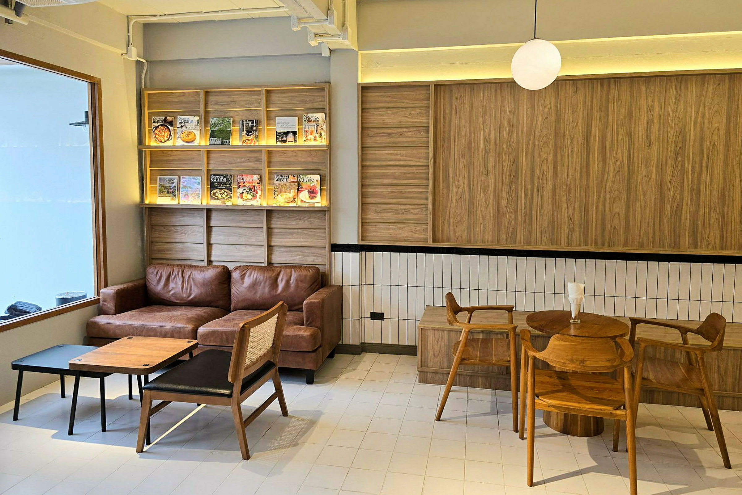 Ett kafé med en brun lädersoffa, träbord och stolar, samt hyllor med böcker och tidskrifter. (AI-genererad text)