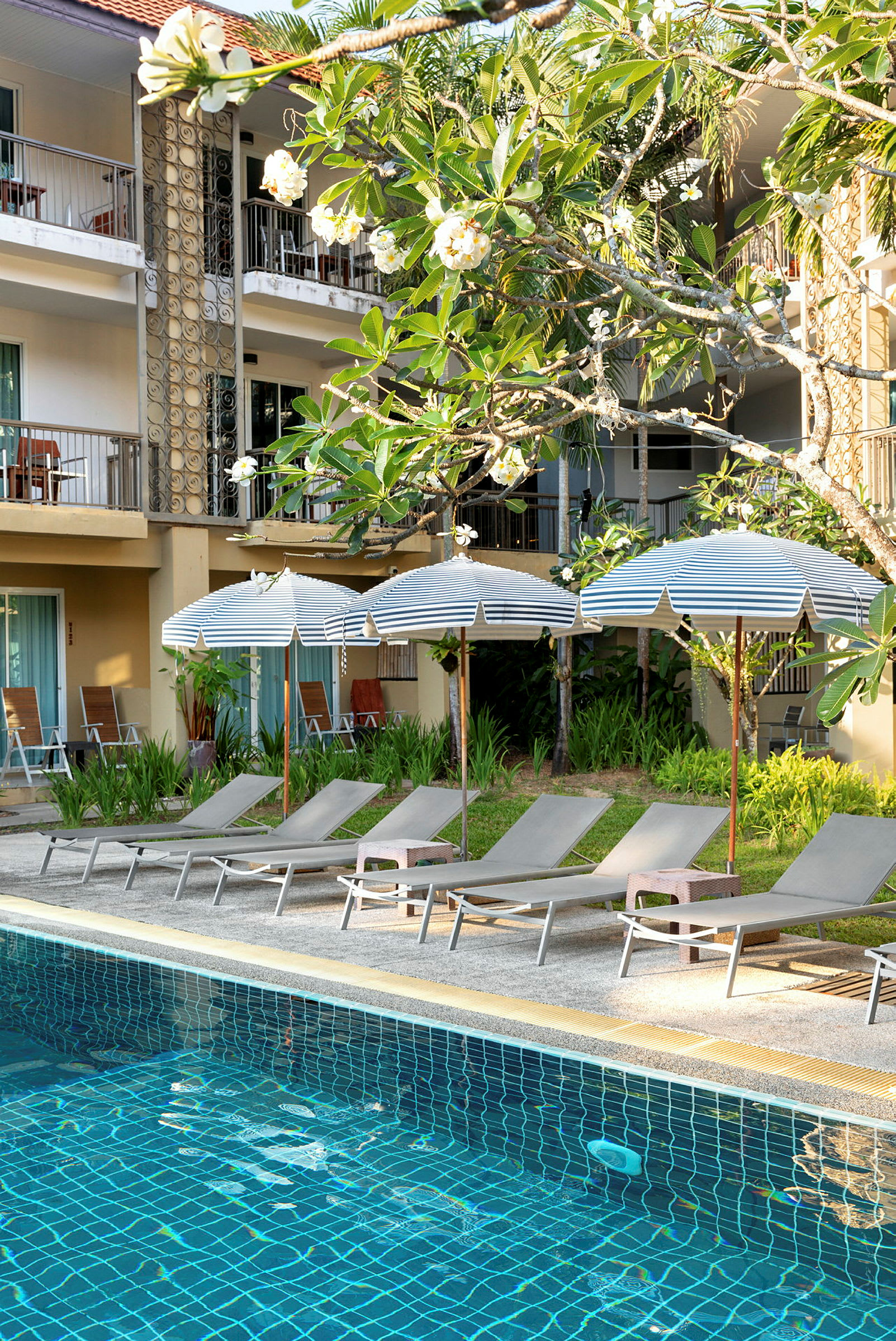 Solstolar och parasoller vid en pool med hotellbyggnad i bakgrunden. (AI-genererad text)