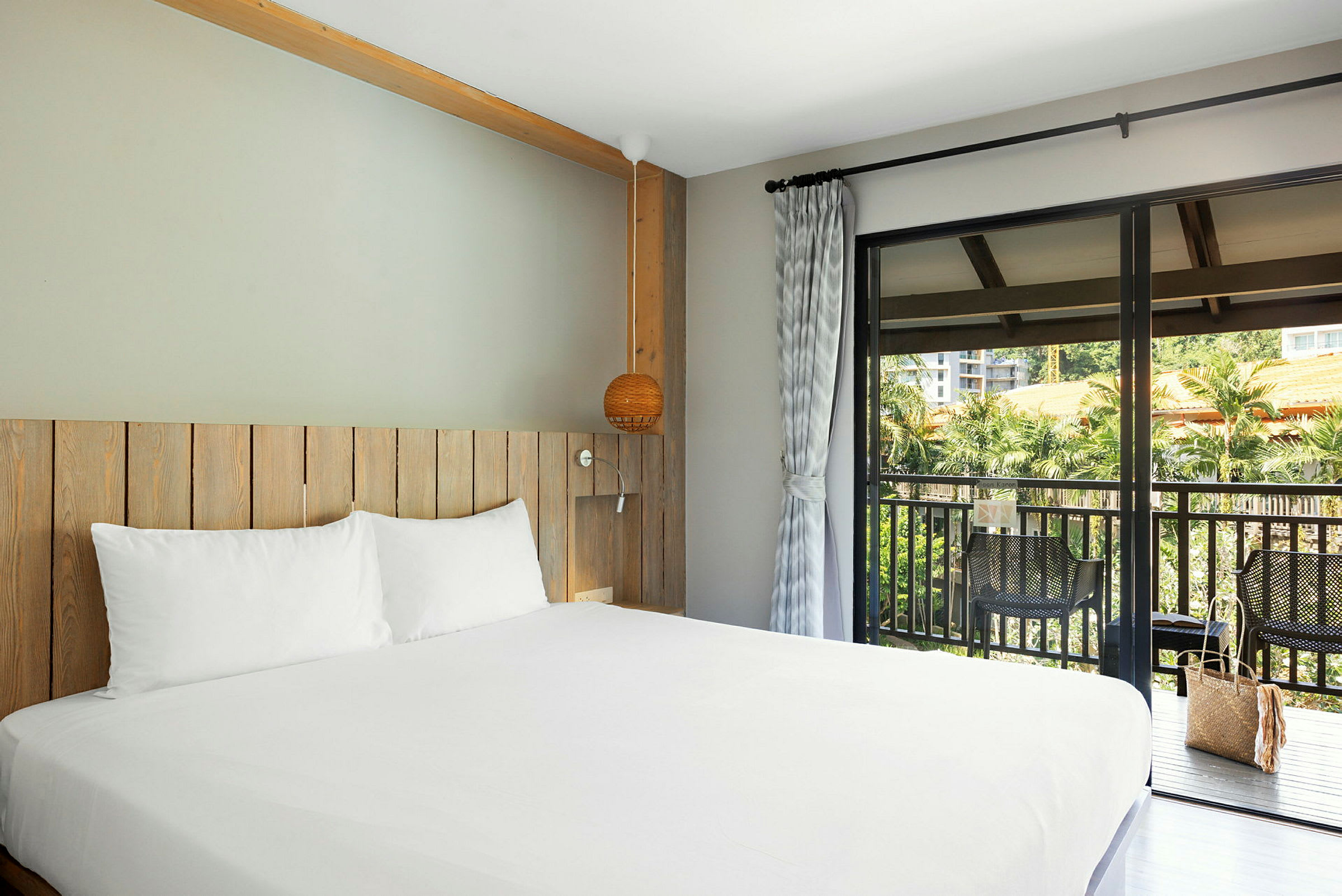 Bild på ett hotellrum med möbler i trä och en säng med vita lakan. En balkong med utsikt finns utanför. (AI-genererad text)
